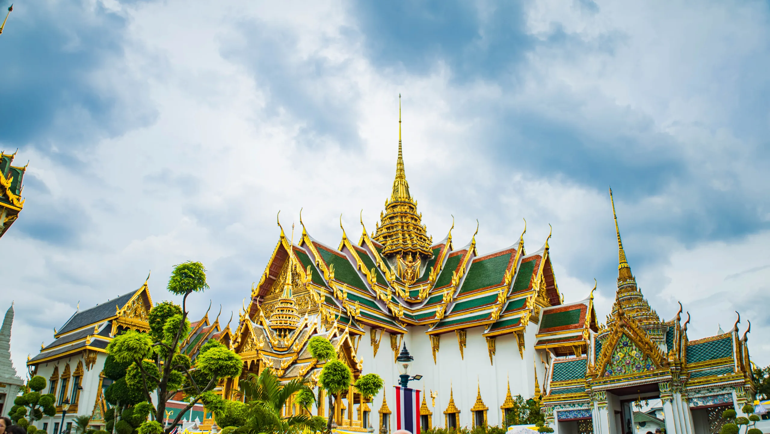 Wielki Pałac w Bangkoku – tradycyjna tajska architektura z bogatymi złotymi zdobieniami i zielonymi dachami, pod pochmurnym niebem