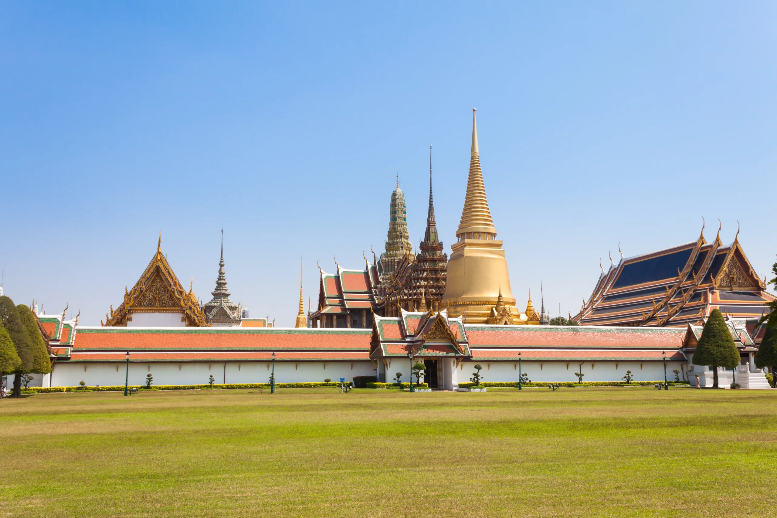 Wat Phra Kaew w Bangkoku – kompleks świątynny z bogato zdobionymi dachami, złotą stupą i tradycyjną tajską architekturą na tle błękitnego nieba