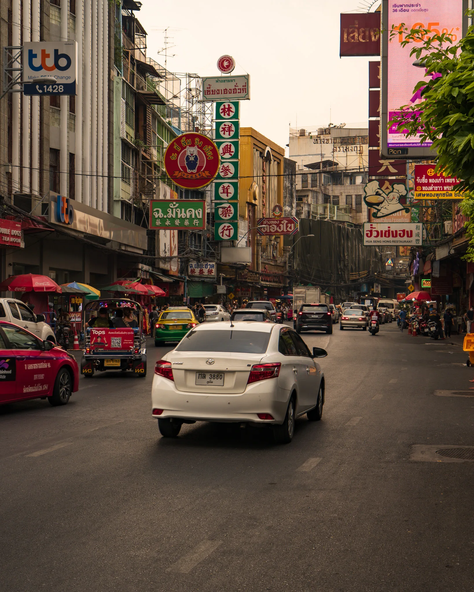 Ruchliwa ulica w dzielnicy Chinatown w Bangkoku z samochodami, tuk-tukami i kolorowymi szyldami w języku chińskim
