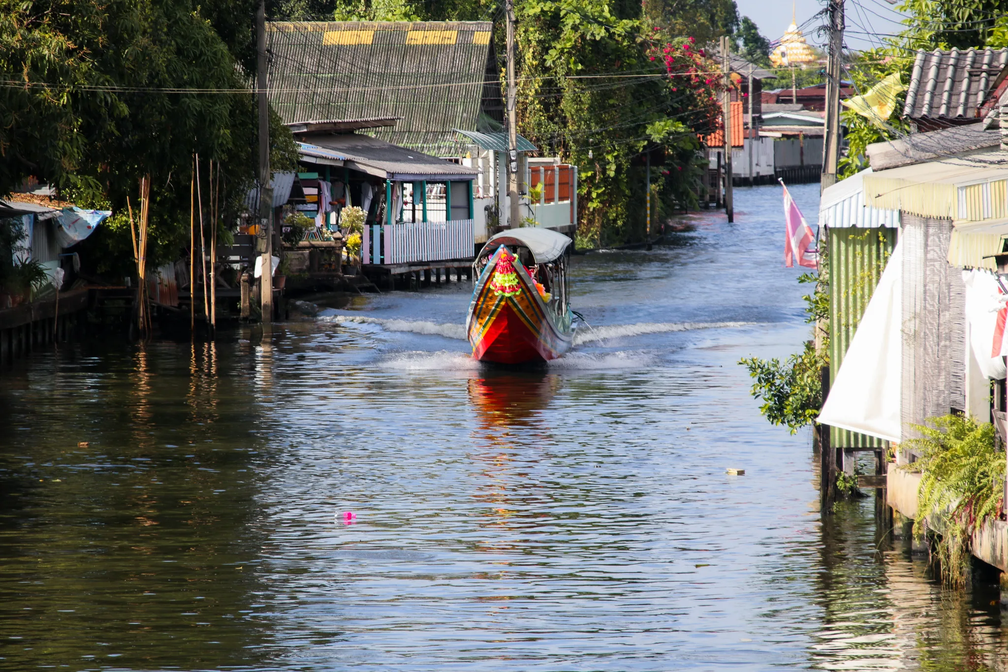 Łódź typu long-tail płynąca kanałem w Bangkoku, mijająca tradycyjne domy nad wodą