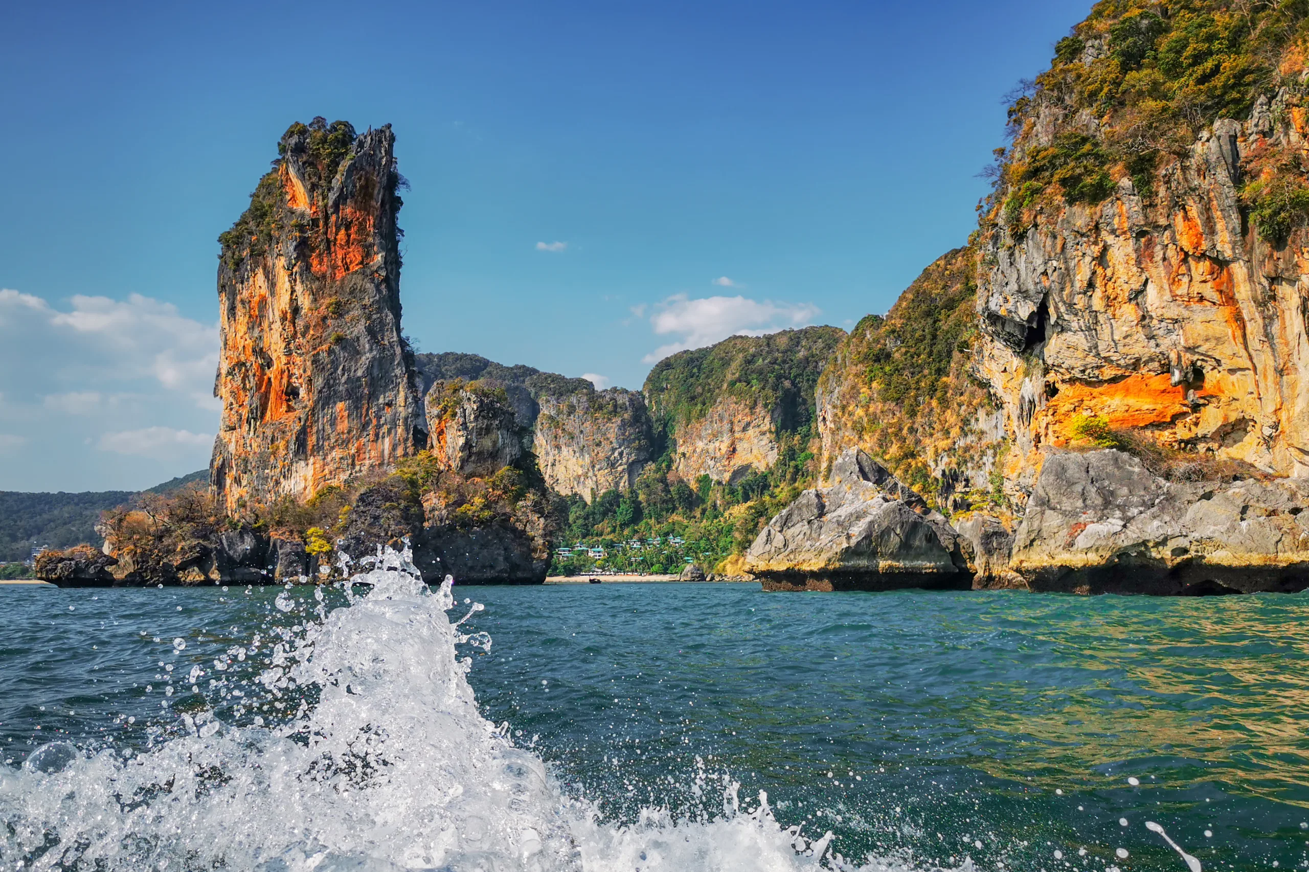 Wysoka wapienna skała wyrastająca z morza w okolicach Railay Beach w Tajlandii, widok z łodzi z rozbryzgującą wodą na pierwszym planie