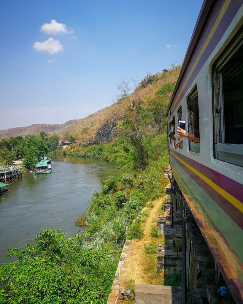 Pociąg jadący wzdłuż rzeki Kwai w Tajlandii, z pasażerami wyglądającymi przez okno