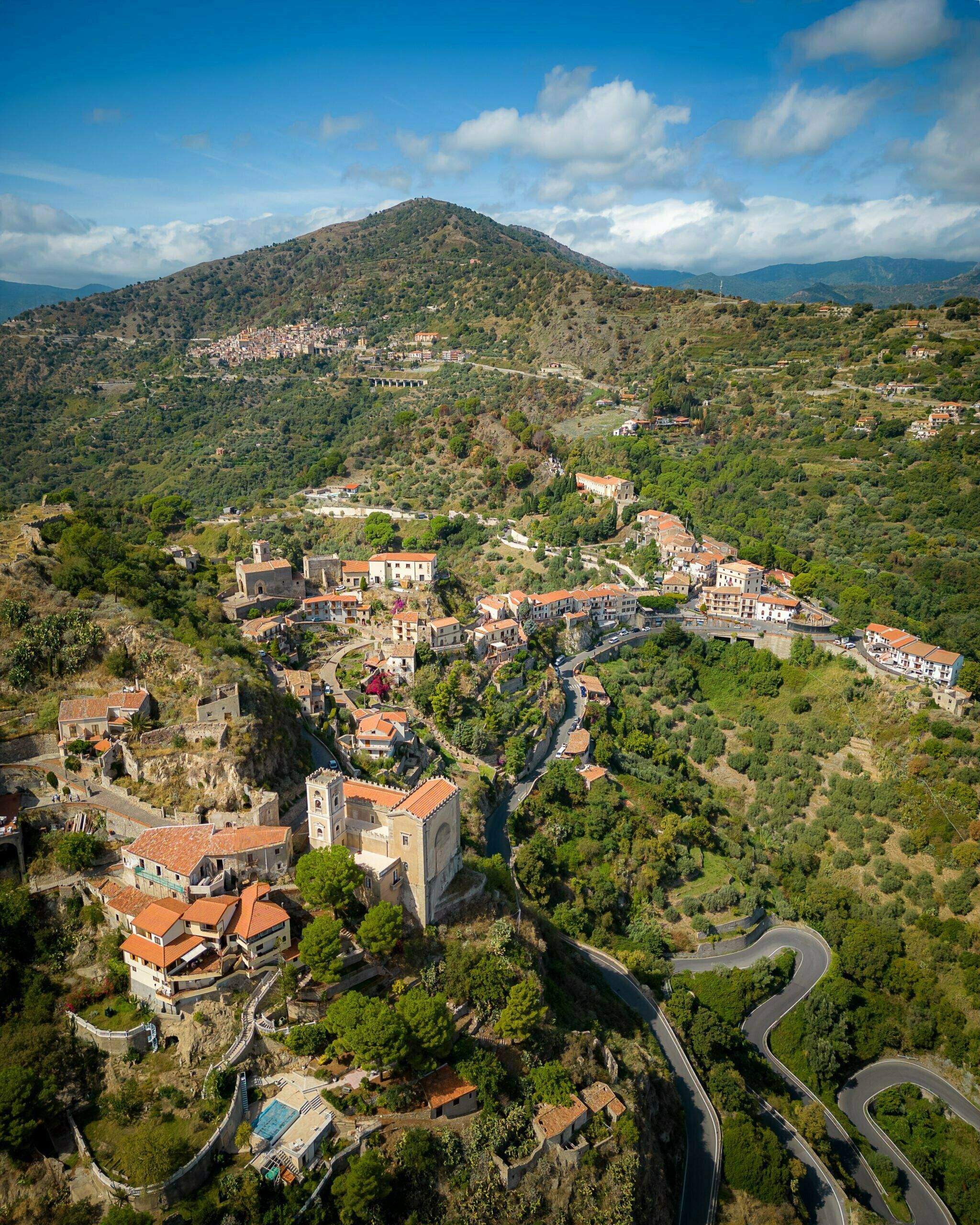 Widok z lotu ptaka na malownicze, górzyste miasteczko z krętymi drogami i czerwonymi dachami, położone wśród zielonych wzgórz na Sycylii, Włochy