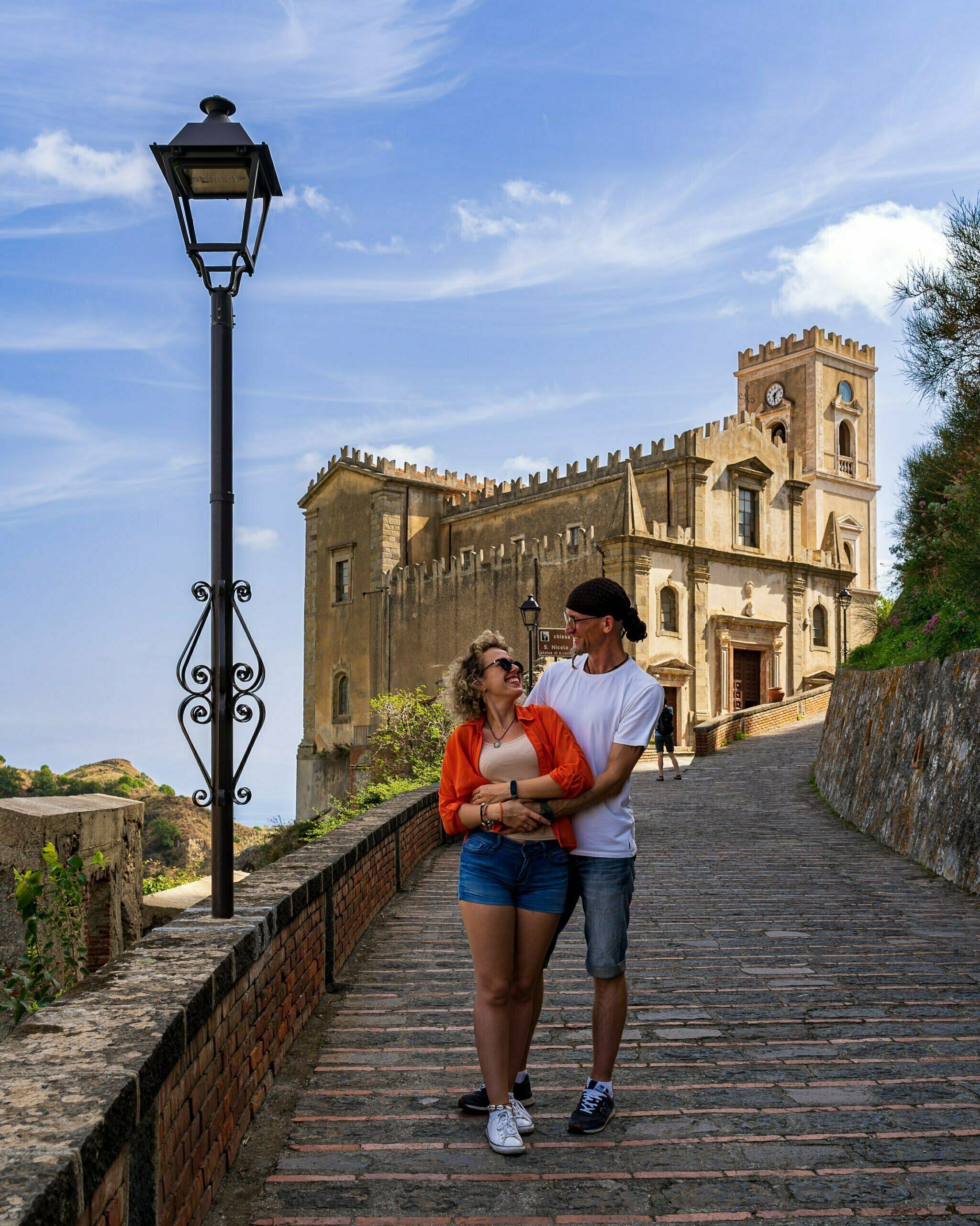 Spacerująca para na brukowanej uliczce w Savoca na Sycylii, z widokiem na zabytkowy kościół San Nicolò