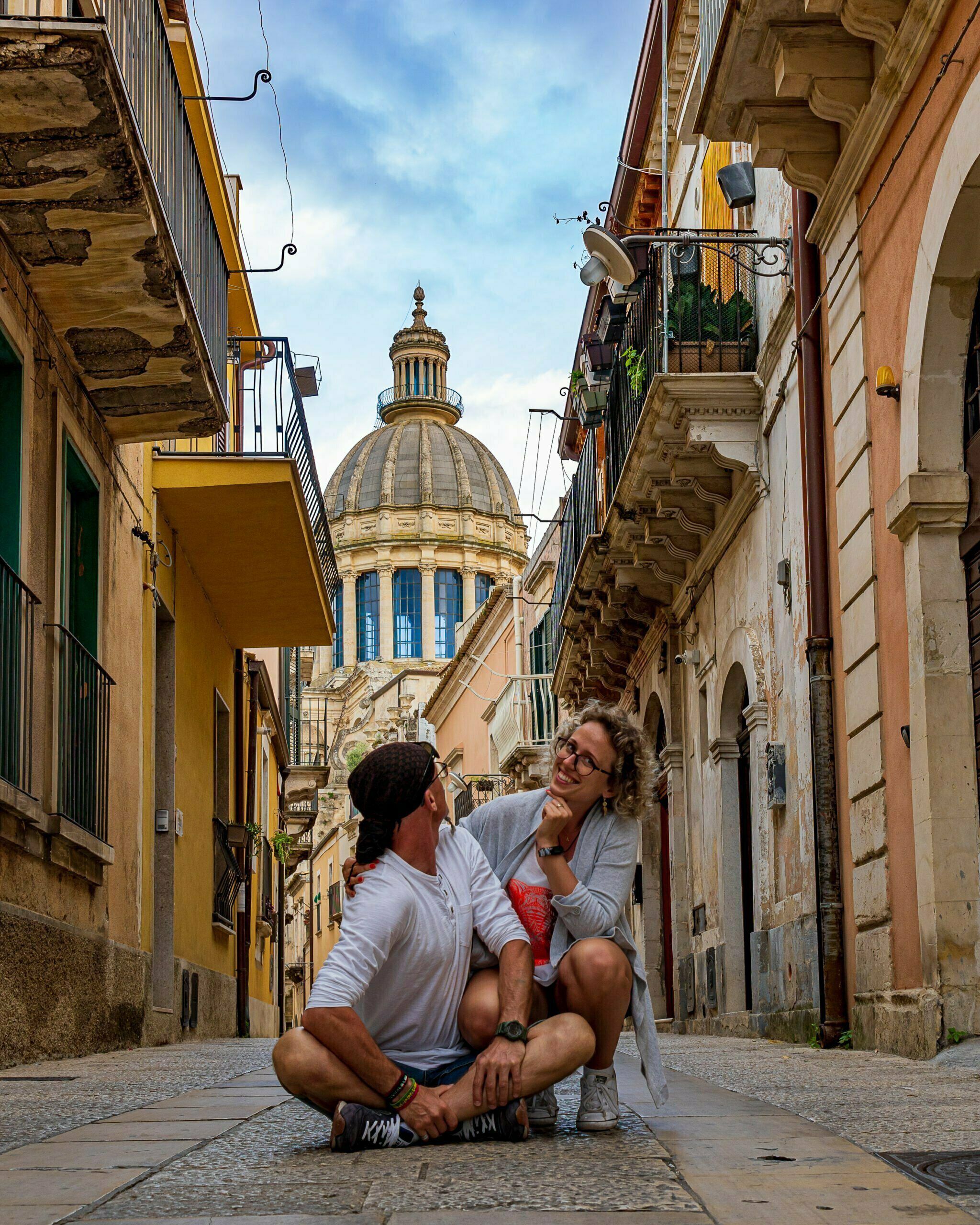 Para siedząca w wąskiej uliczce Ragusa Ibla z widokiem na kopułę katedry San Giorgio