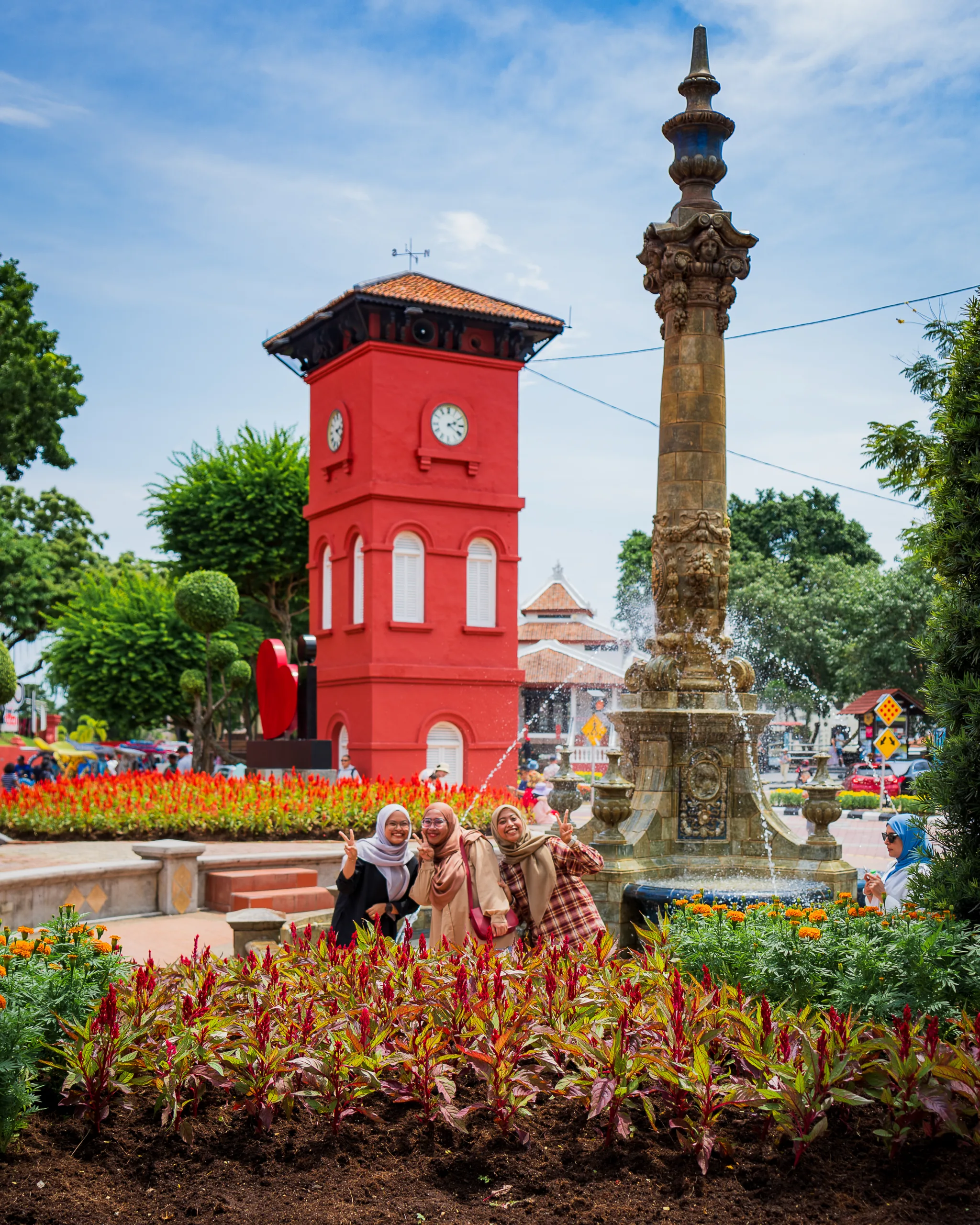 Grupa uśmiechniętych kobiet pozujących przy fontannie na placu Dutch Square w Malakka, w tle charakterystyczna czerwona wieża zegarowa.