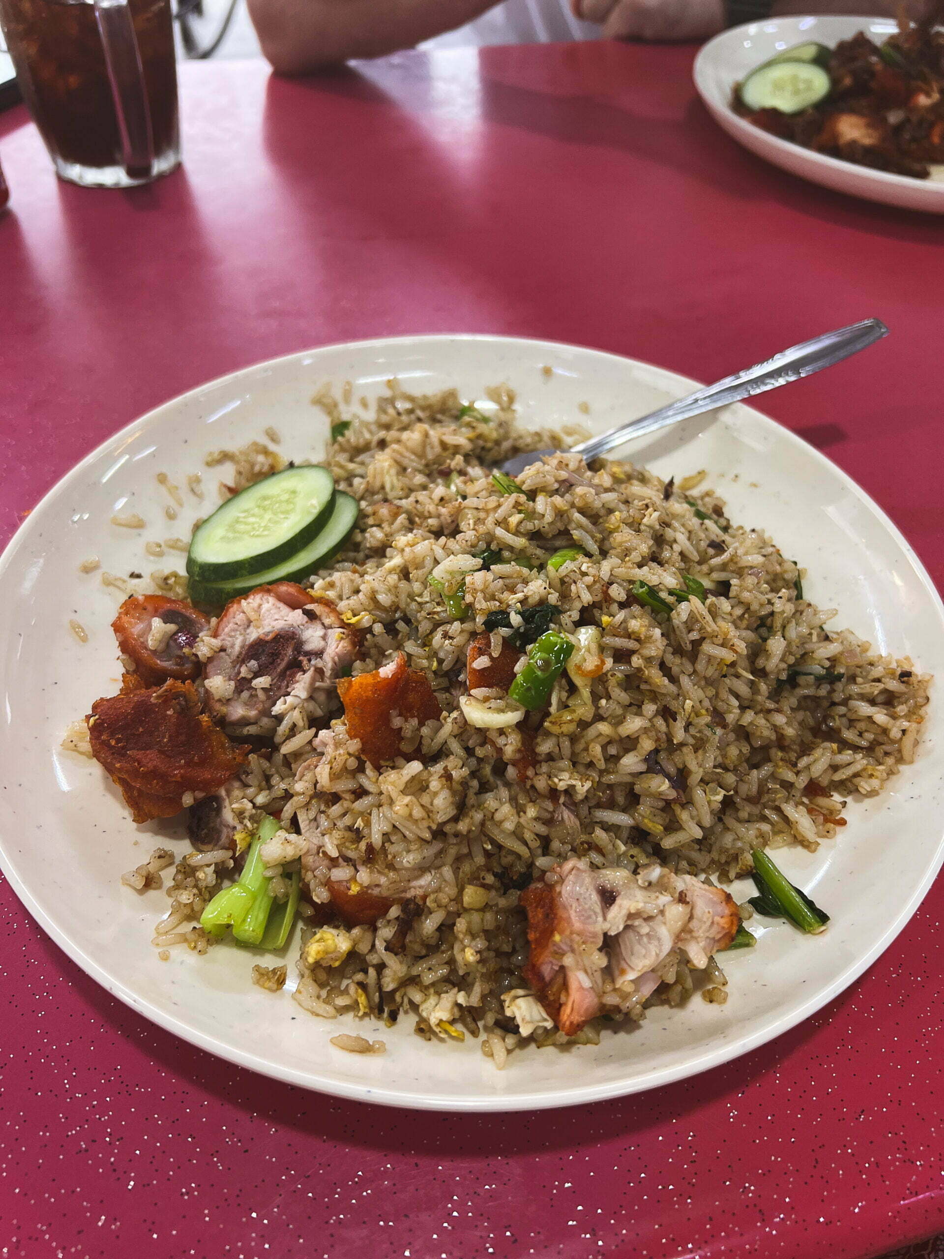 Talerz smażonego ryżu z kawałkami pieczonego kurczaka, zieloną cebulką i plasterkami ogórka, podany na białym talerzu - nasi goreng - Kuchnia Malezyjska