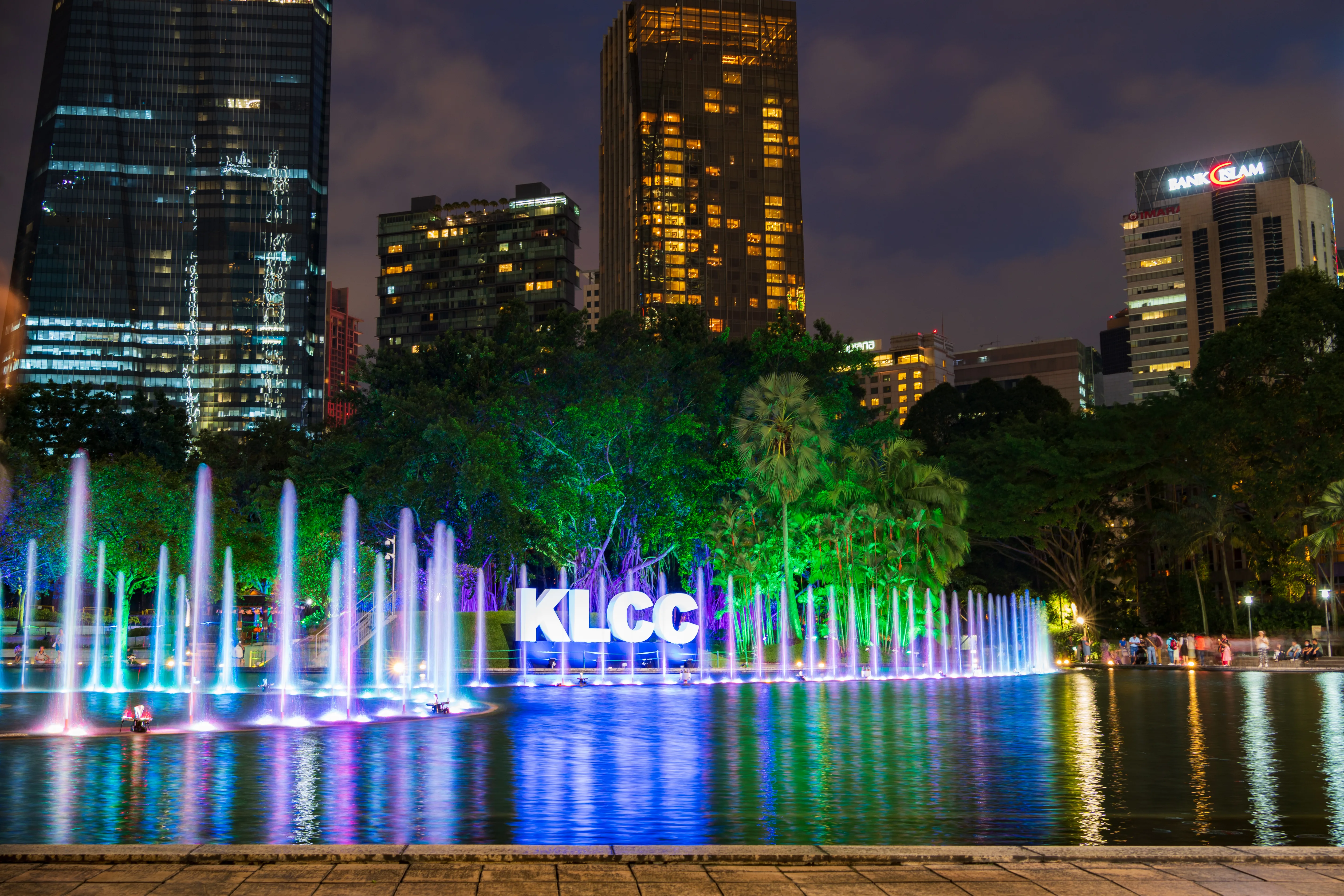 Kolorowe fontanny KLCC nocą w centrum Kuala Lumpur w Malezji, otoczone podświetlonymi wieżowcami.