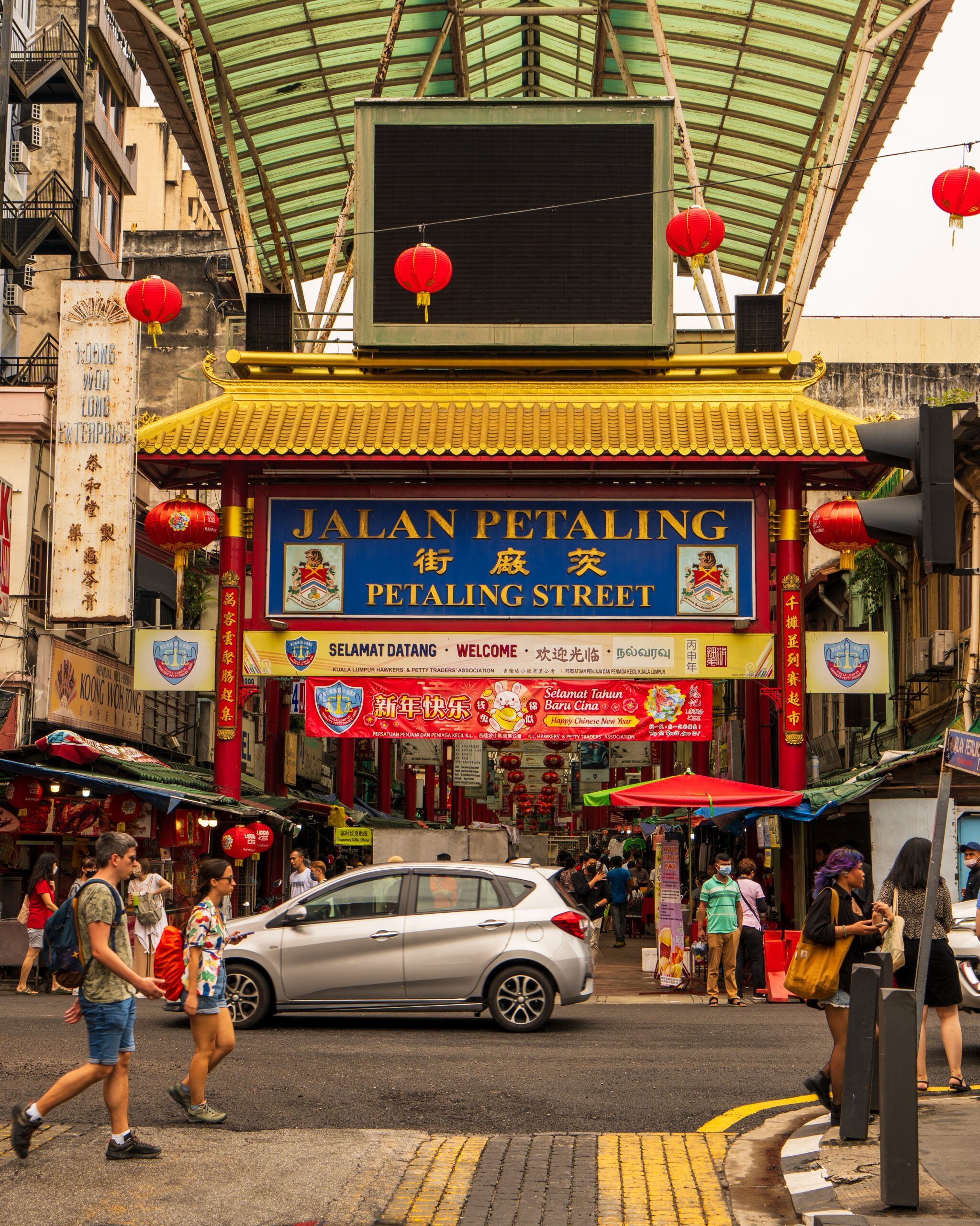 Wejście do Petaling Street w Kuala Lumpur z charakterystyczną złotą bramą, czerwonymi lampionami i tłumem przechodniów.