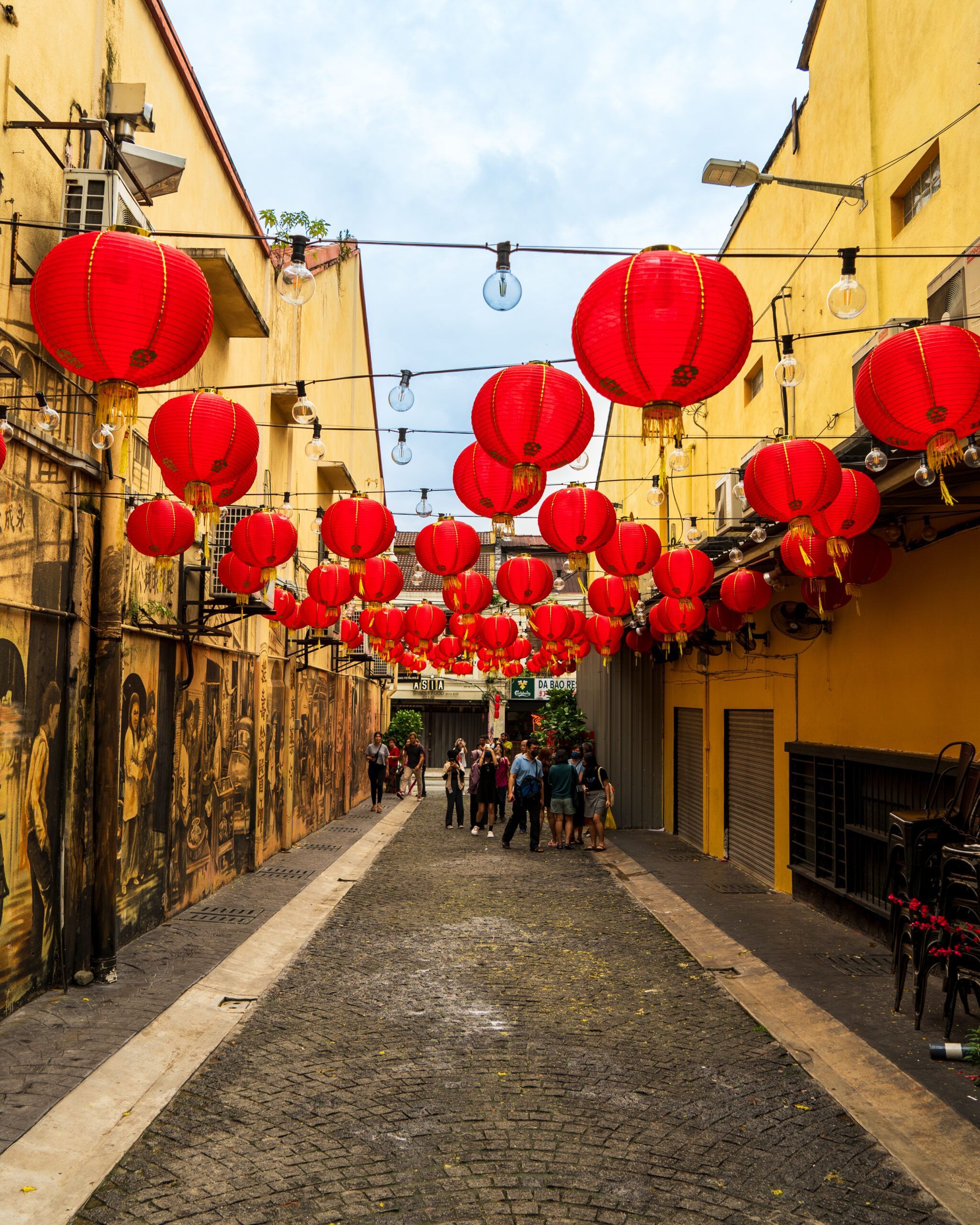 Ulica w Chinatown w Kuala Lumpur udekorowana licznymi czerwonymi lampionami, z muralami na ścianach i spacerującymi ludźmi.