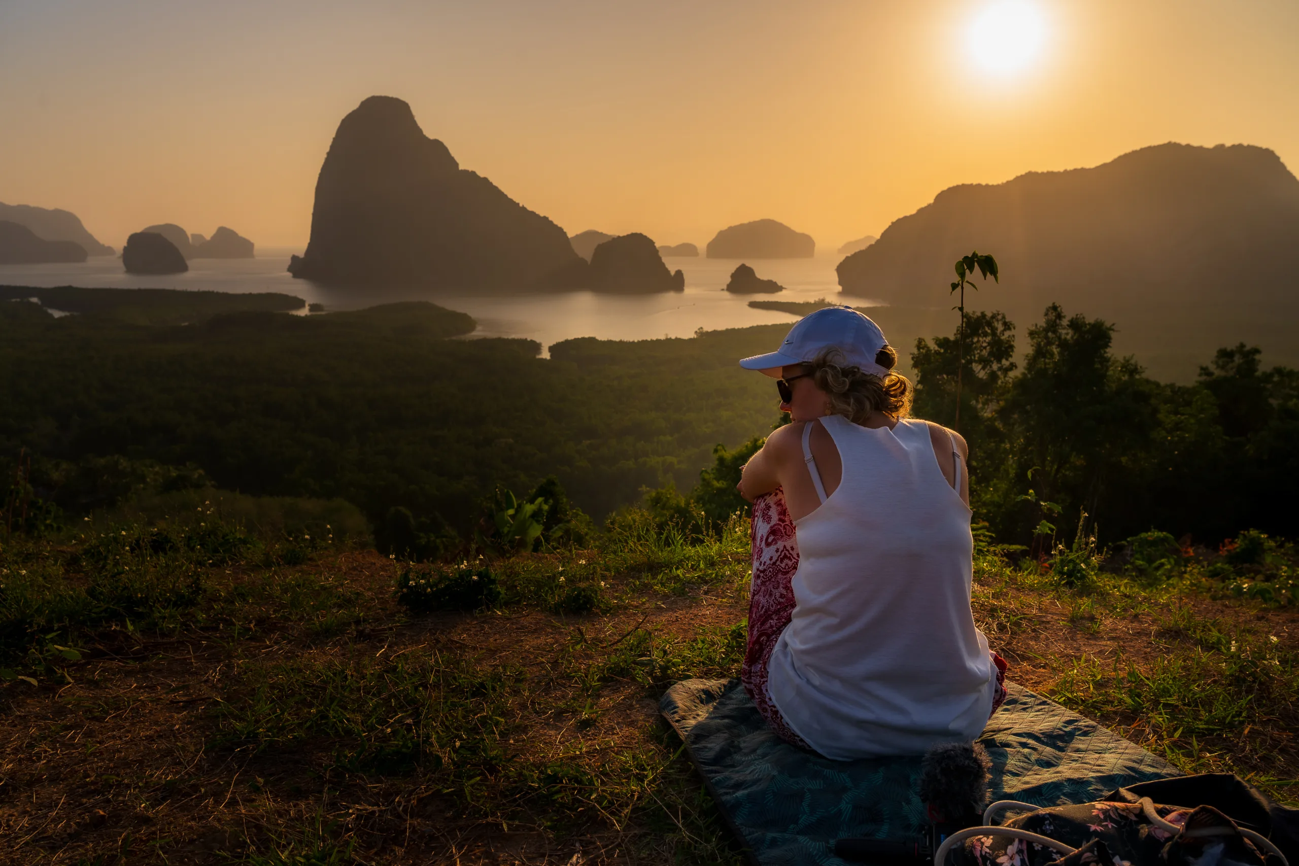 Kobieta siedząca na kocu, patrząca na zachód słońca nad zatoką i wyspami porośniętymi zielenią