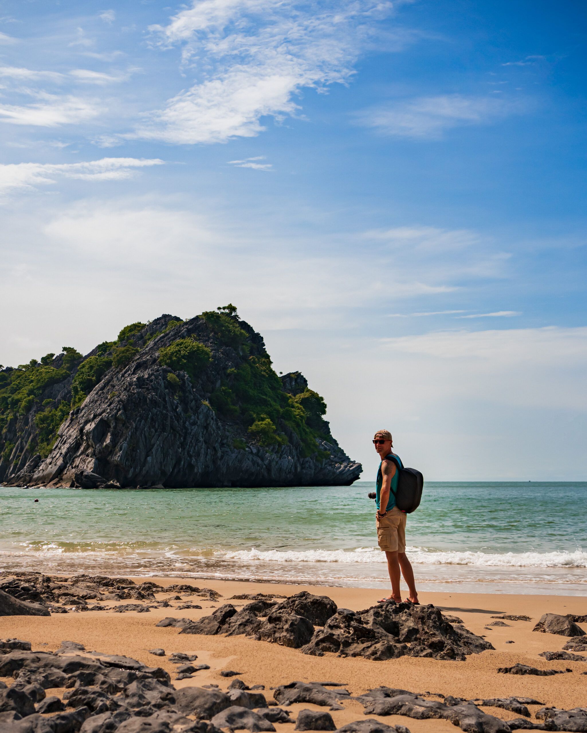 Turysta z plecakiem na pustej plaży na wyspie Cát Bà w Wietnamie – w tle wapienne wzgórze porośnięte zielenią i spokojne morze
