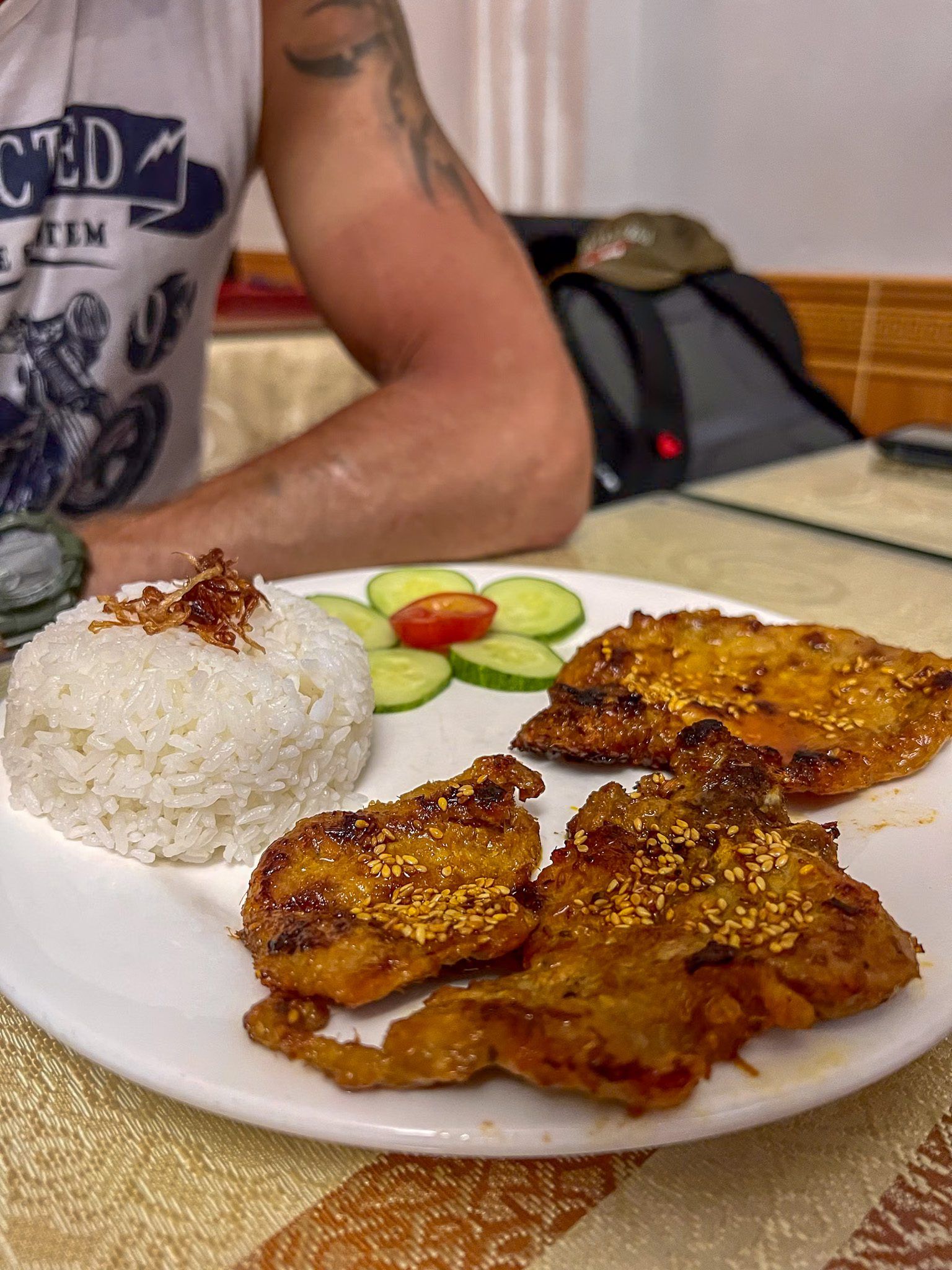 Talerz z grillowaną wieprzowiną posypaną sezamem, porcją ryżu i plasterkami ogórka i pomidora