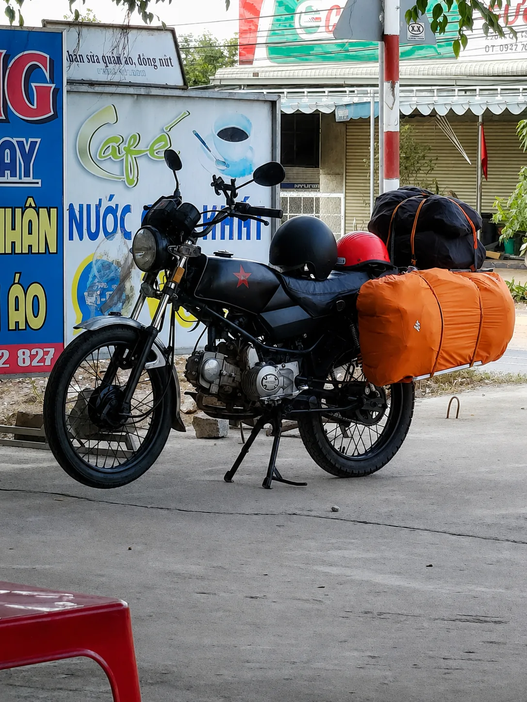 Motocykl z bagażem przygotowany do podróży po Wietnamie, zaparkowany przed przydrożną kawiarnią.