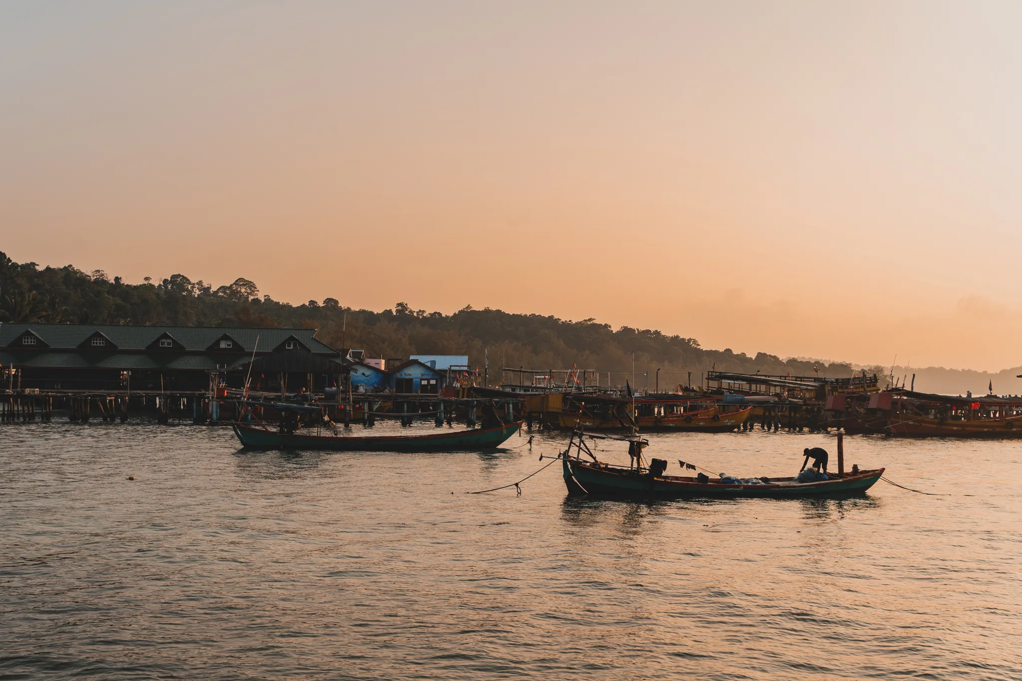 Łodzie rybackie na tle zachodu słońca w porcie na wyspie Koh Rong, Kambodża.