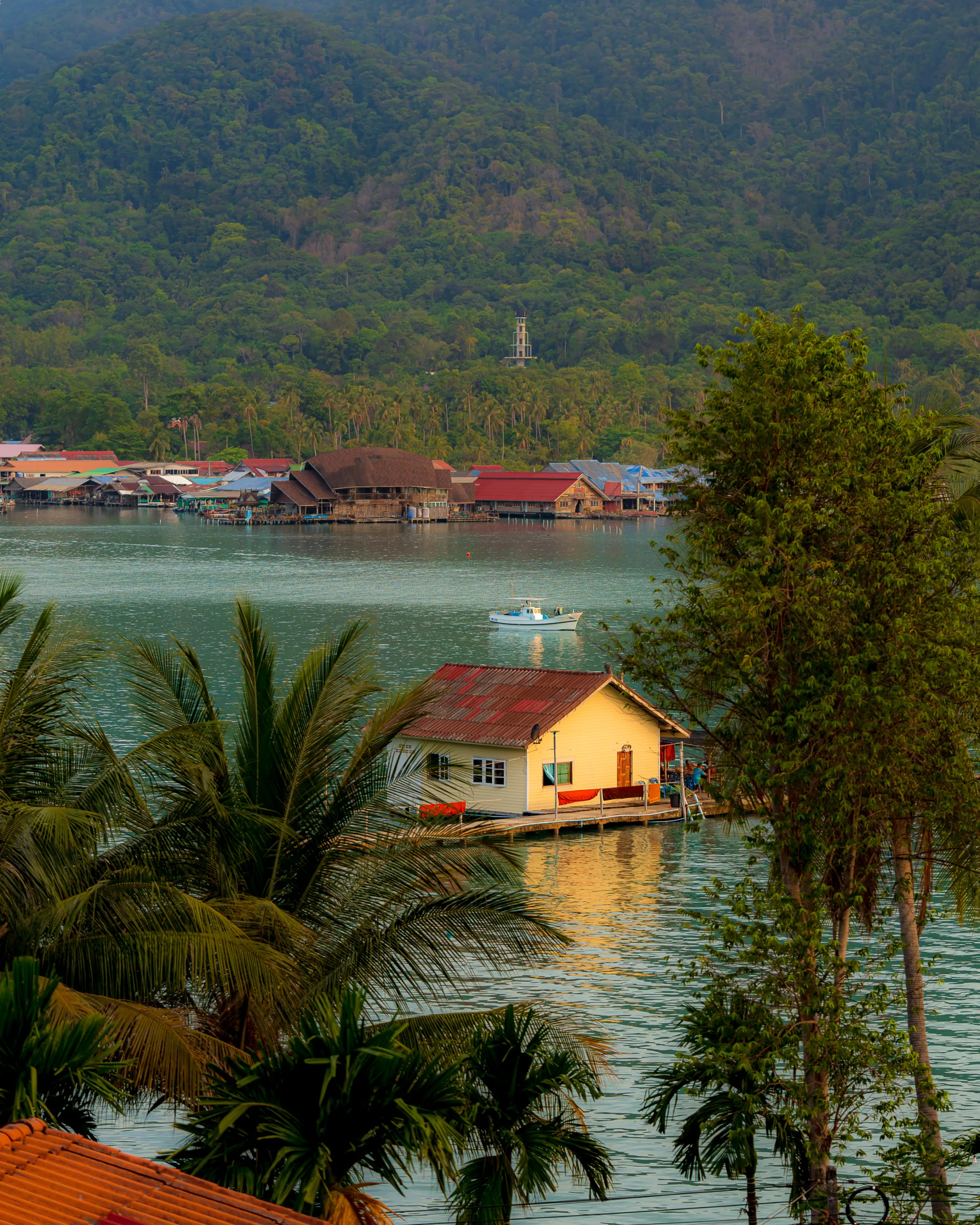 Drewniany domek na wodzie w tropikalnej scenerii z palmami i górami w tle – spokojna wioska rybacka w Tajlandii