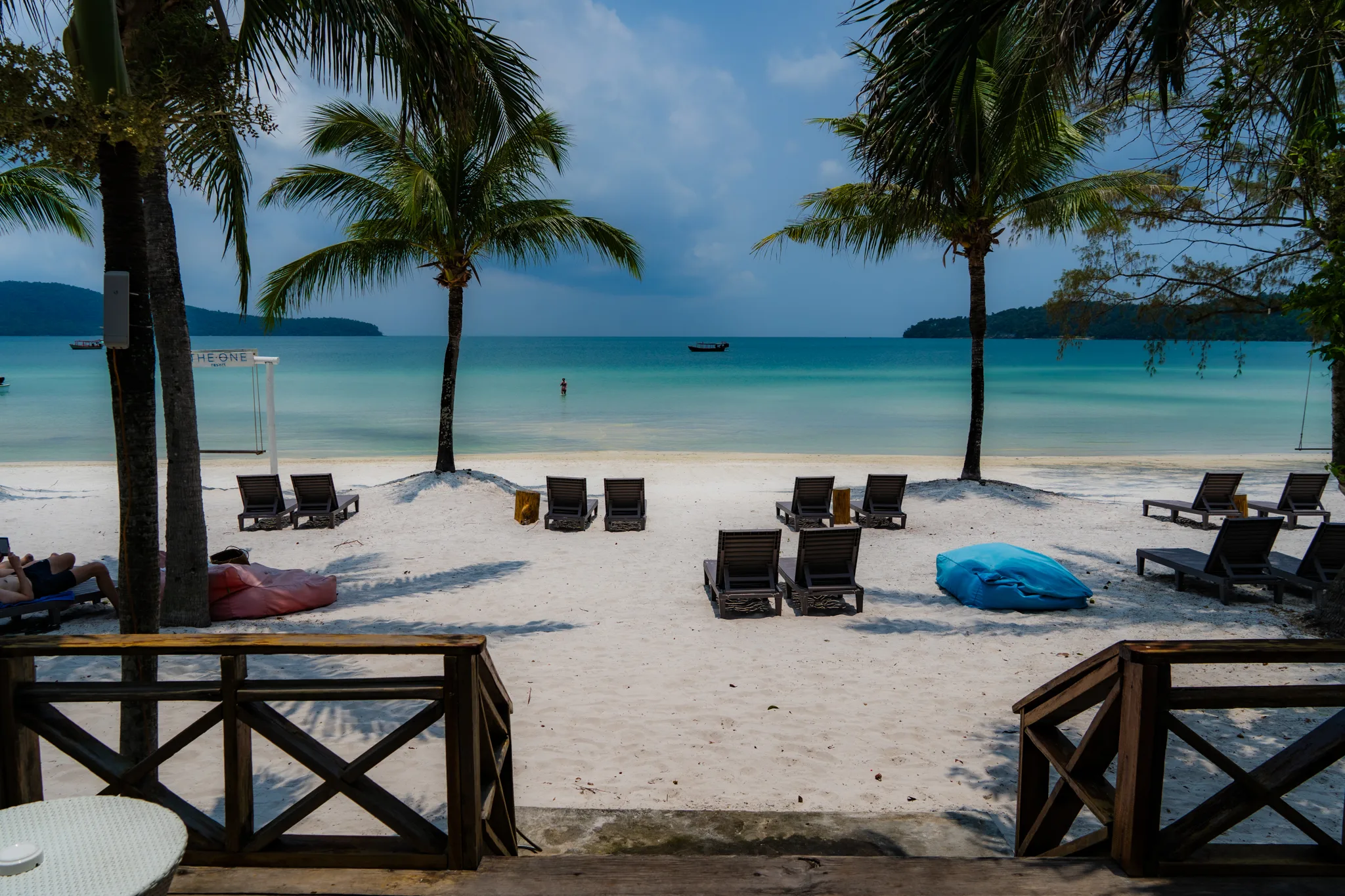 Leżaki na białej plaży z widokiem na turkusowe morze i palmy, Koh Rong, Kambodża.