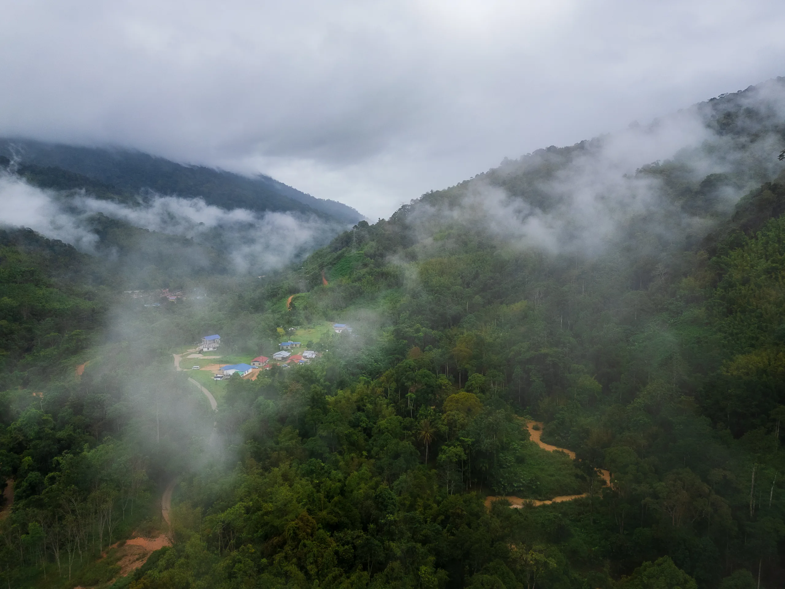 Widok na górską dolinę spowitą mgłą z niewielką osadą wśród zieleni