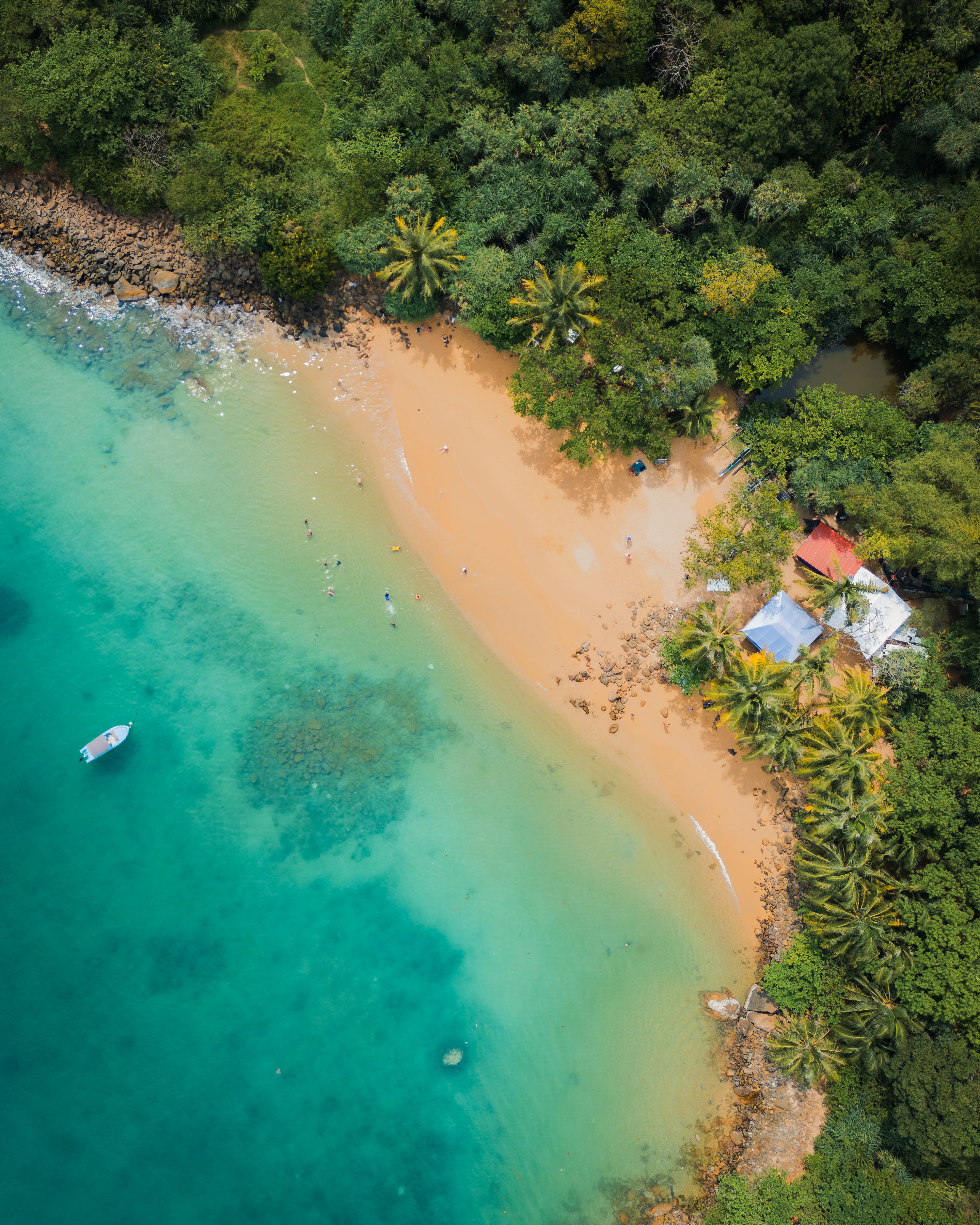 Widok z drona na Unawatuna Beach na Sri Lance, z turkusową wodą, piaszczystą plażą i palmami otaczającymi zatokę.