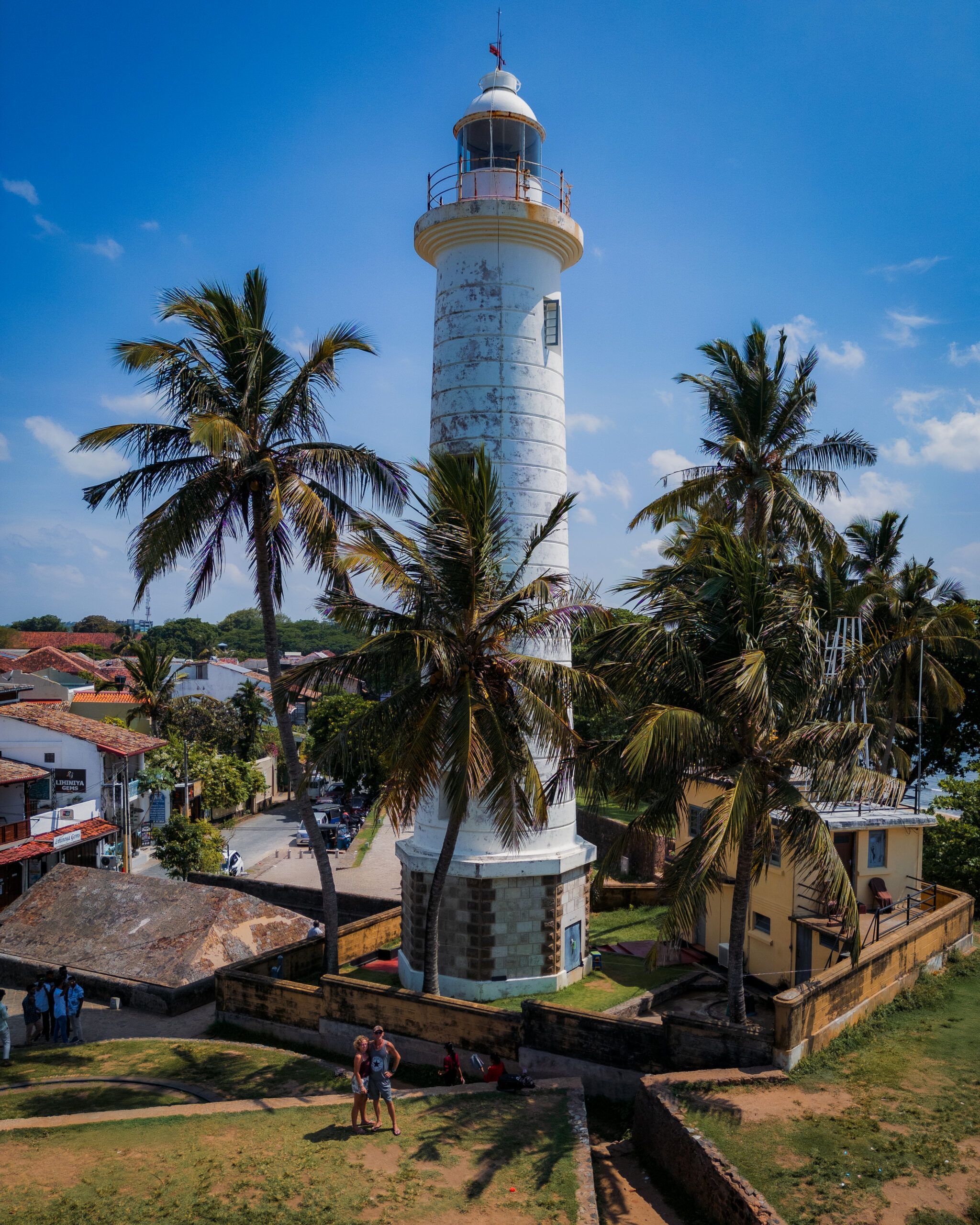 Biała latarnia morska w forcie Galle na Sri Lance, otoczona palmami i kolonialną zabudową.