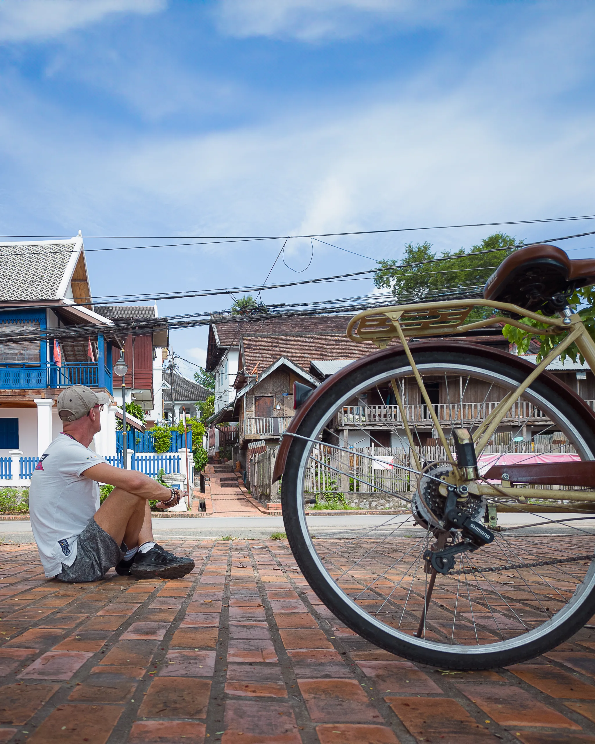 Podróżnik odpoczywający przy rowerze na ulicy w Luang Prabang w Laosie, wśród tradycyjnej zabudowy i kolonialnych domów.