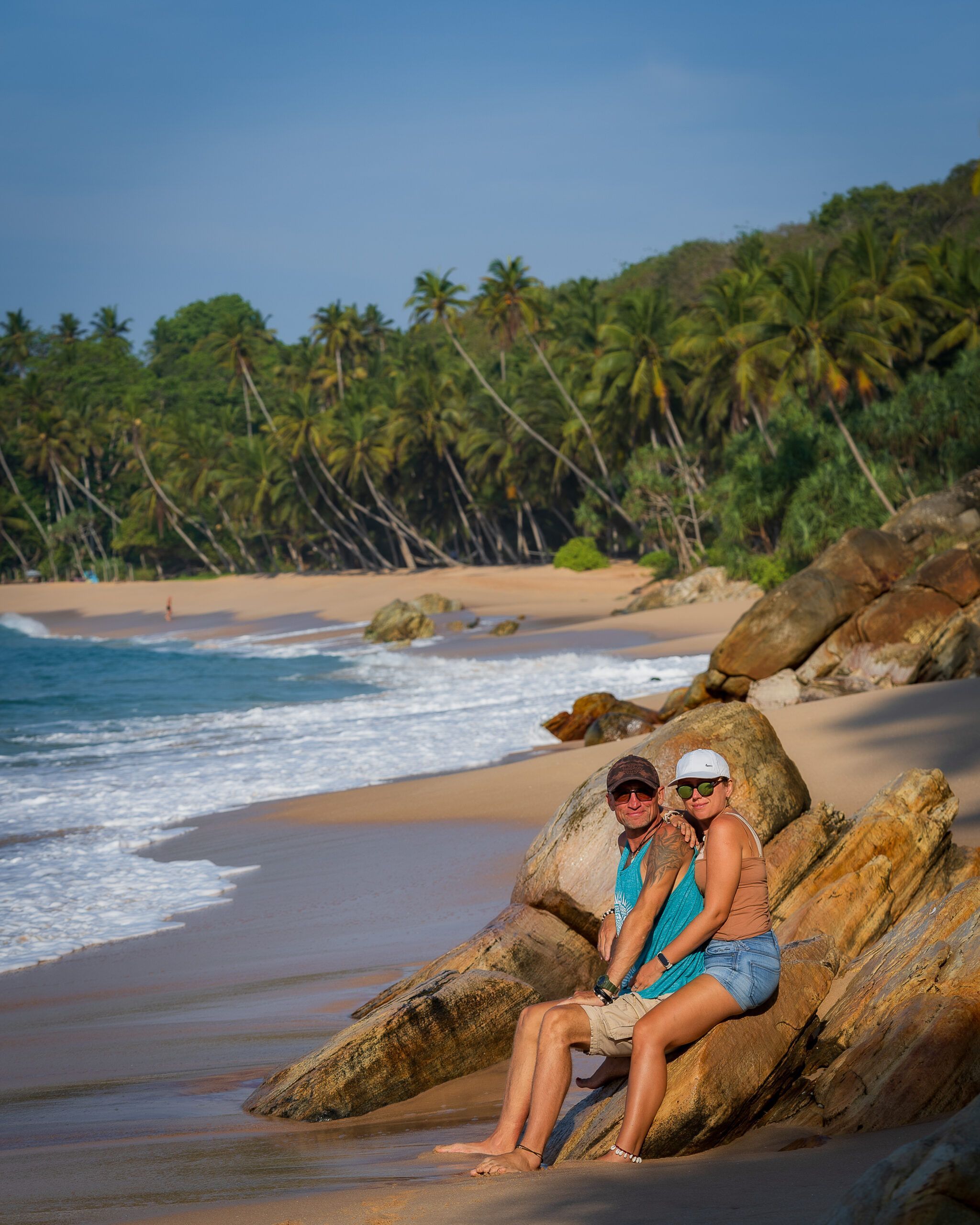 Para siedząca na skałach przy plaży na Sri Lance, w tle rząd pochylonych palm kokosowych i spokojny ocean.
