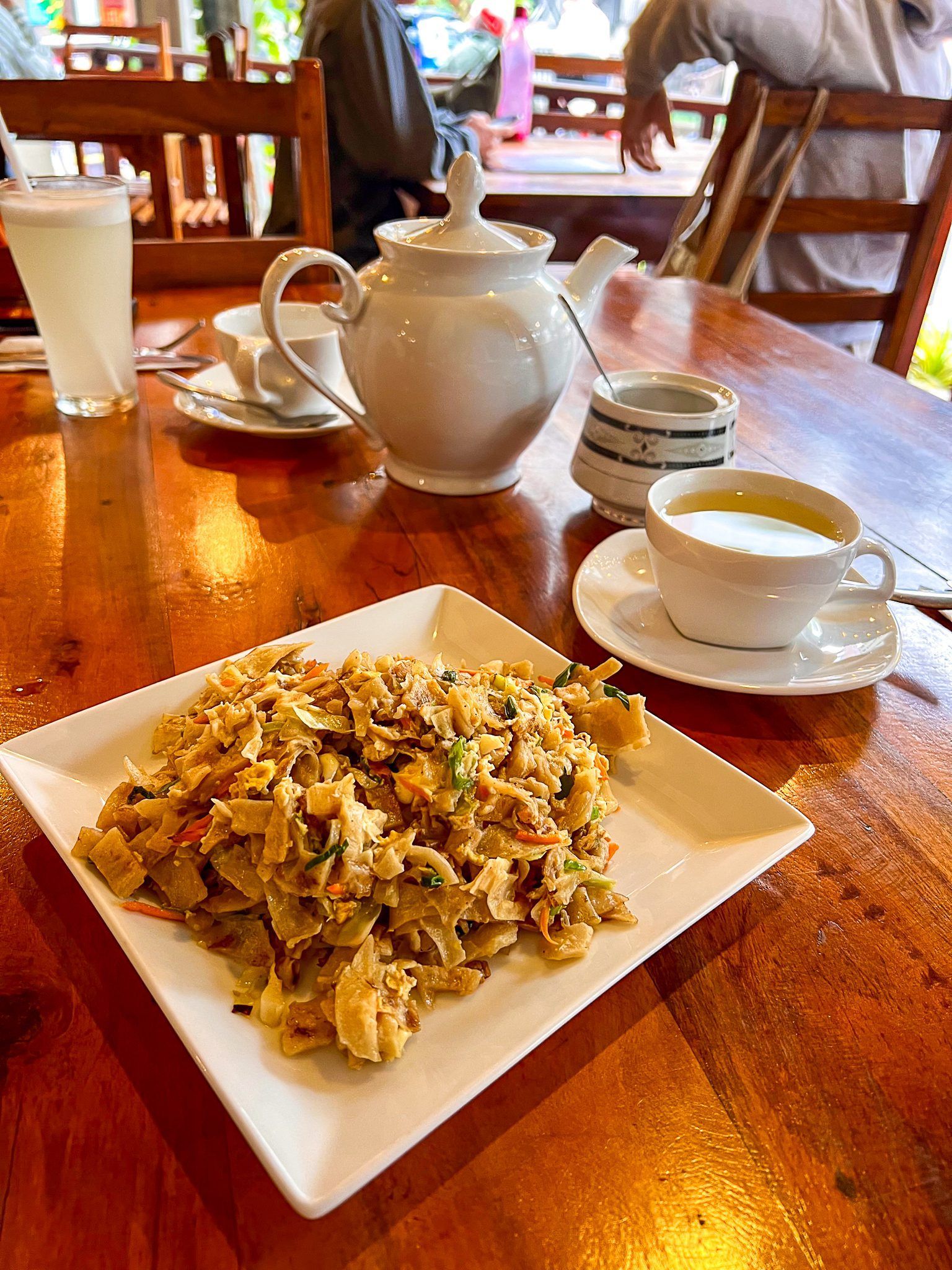 Tradycyjne danie kottu roti podane na białym talerzu w lankijskiej restauracji, obok dzbanek z herbatą i filiżanka.