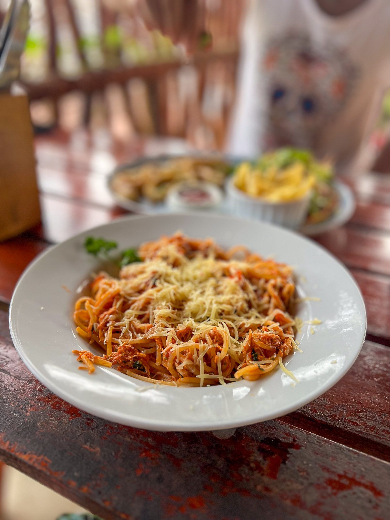 Talerz makaronu spaghetti z sosem pomidorowym i startym serem, podany na drewnianym stole w restauracji.