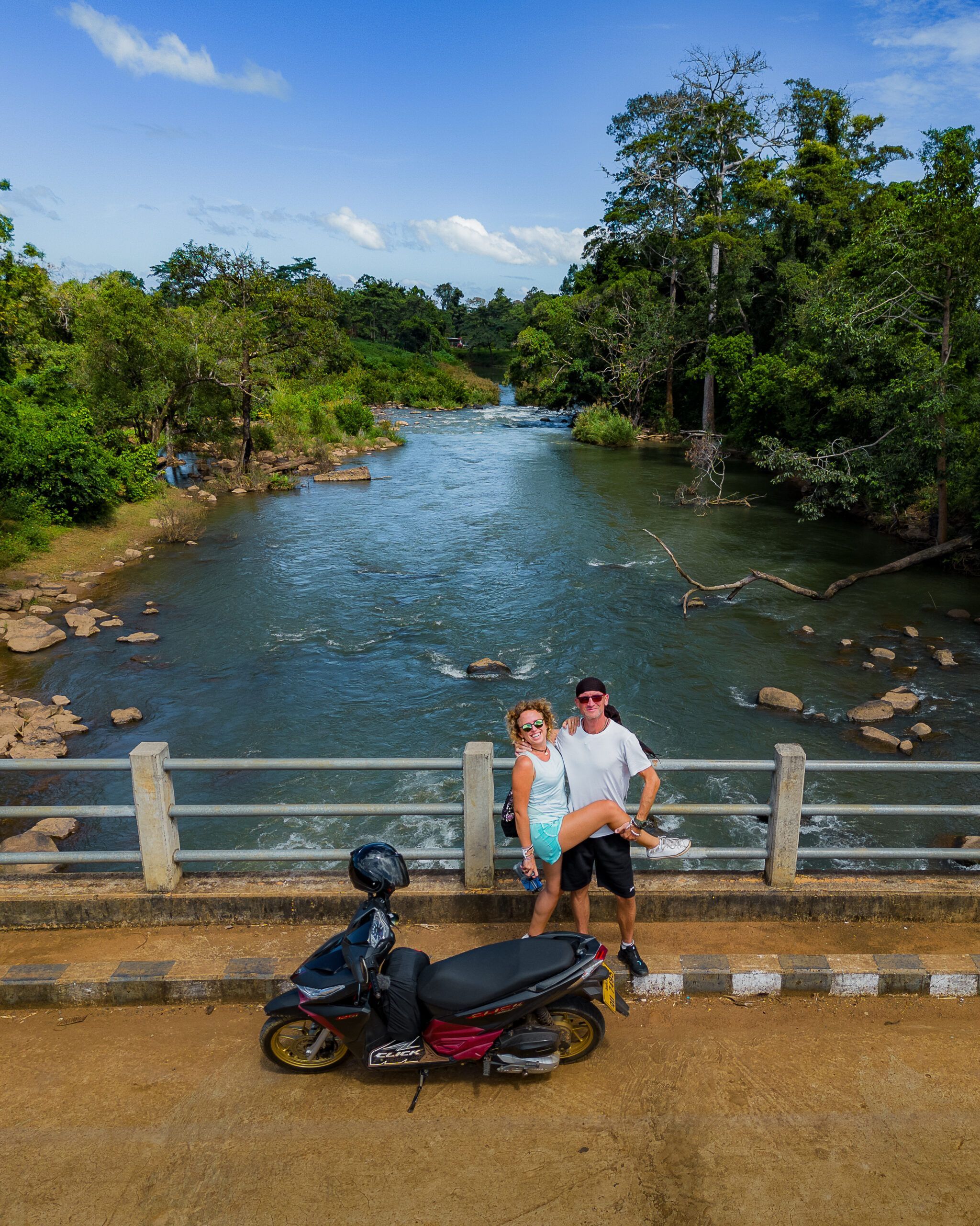 Para turystów pozująca na moście nad rzeką w otoczeniu tropikalnej zieleni, obok zaparkowanego skutera – słoneczny dzień w egzotycznym plenerze - Pętla Pakse