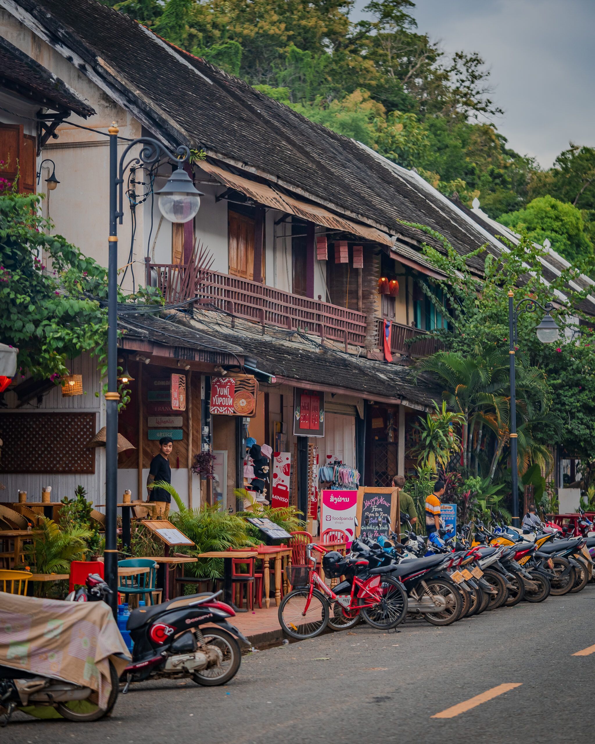 Ulica w Luang Prabang z rzędem skuterów zaparkowanych przed kolorowymi kawiarniami i sklepami w kolonialnych budynkach - co zobaczyć w laosie
