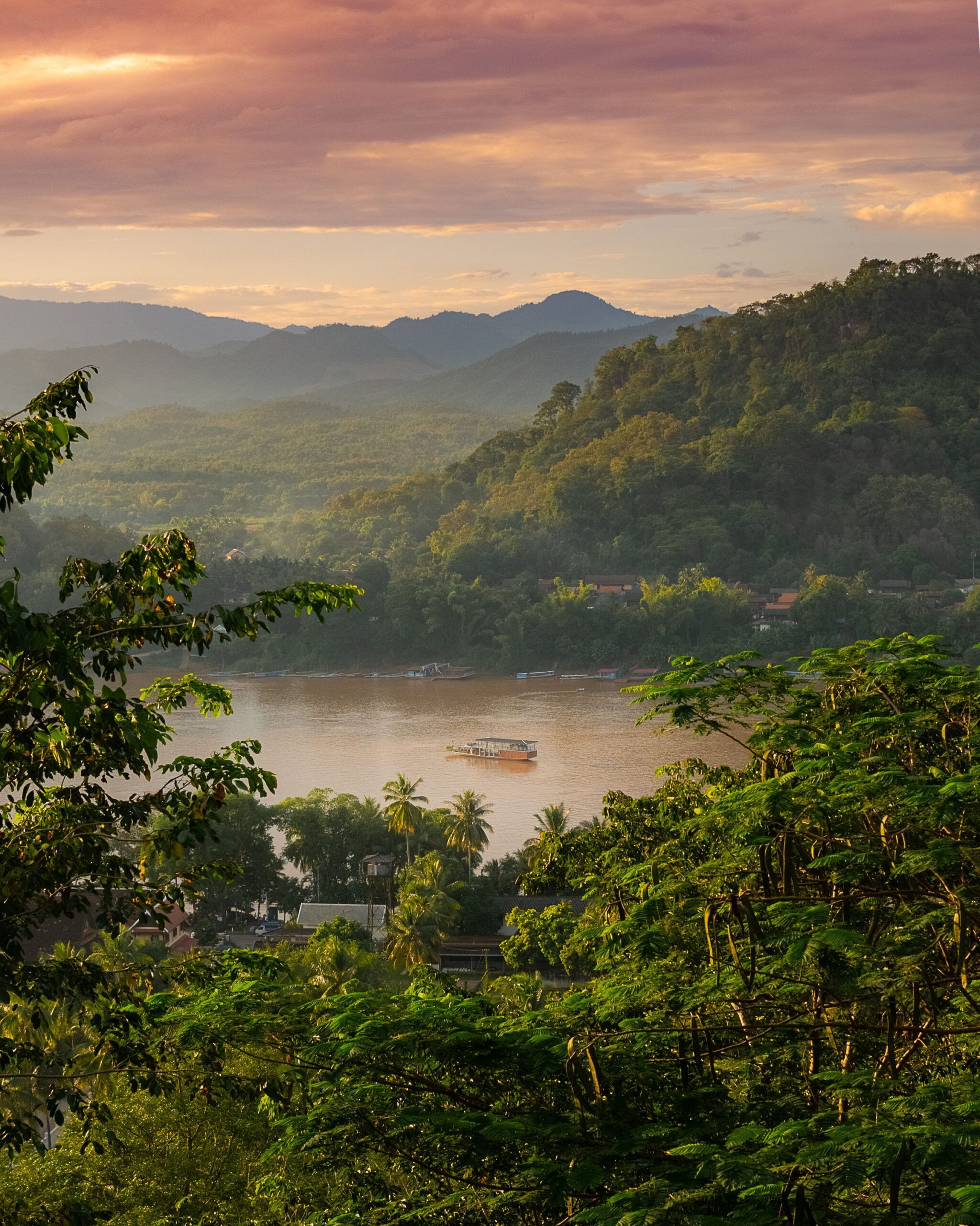 Zachód słońca nad rzeką Mekong w Luang Prabang, z łodzią wycieczkową i górzystym horyzontem w tle.
