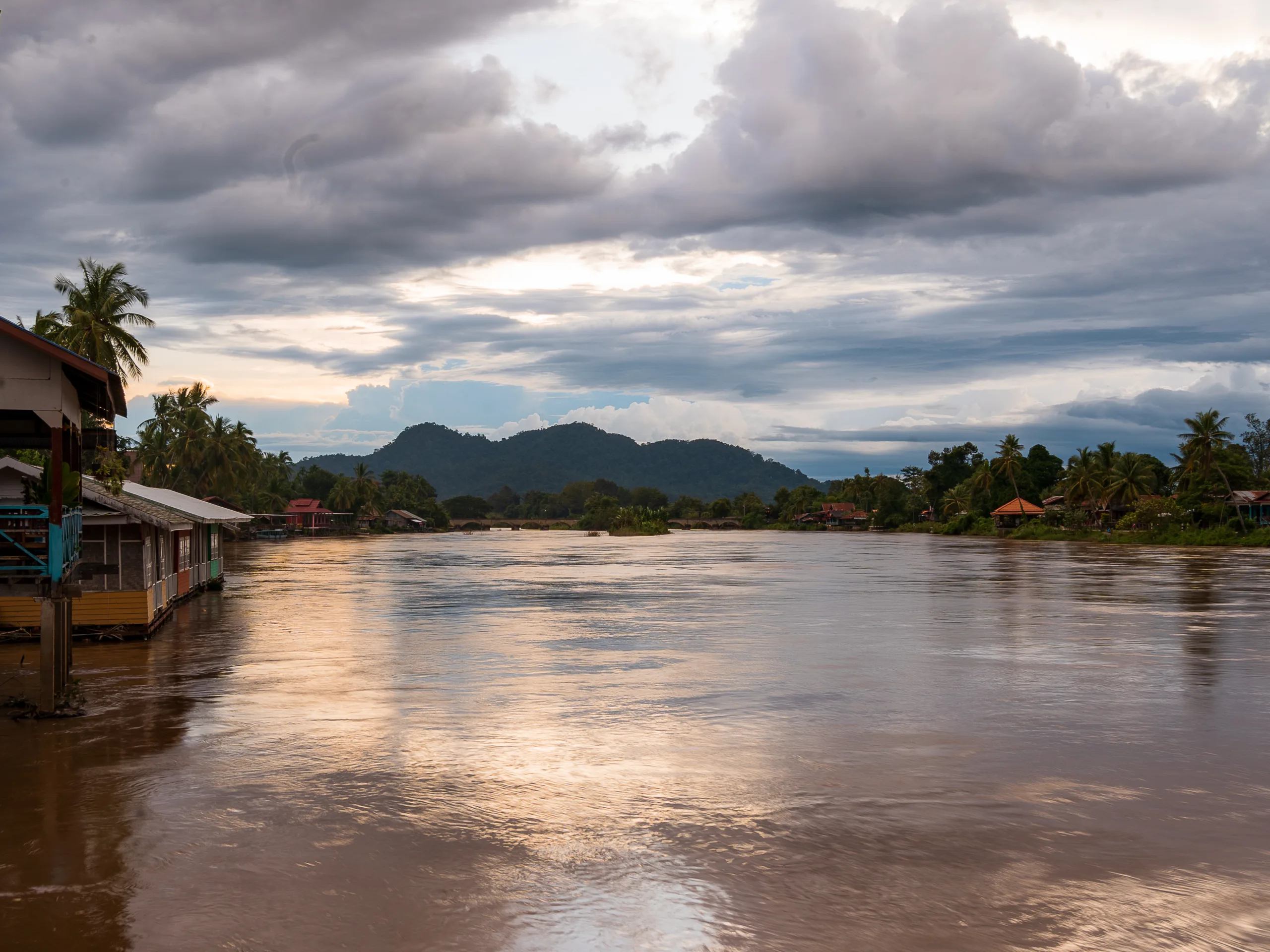 Zachód słońca nad Mekongiem na 4000 wyspach (Si Phan Don) w Laosie – widok na rzekę, palmy i drewniane domki.