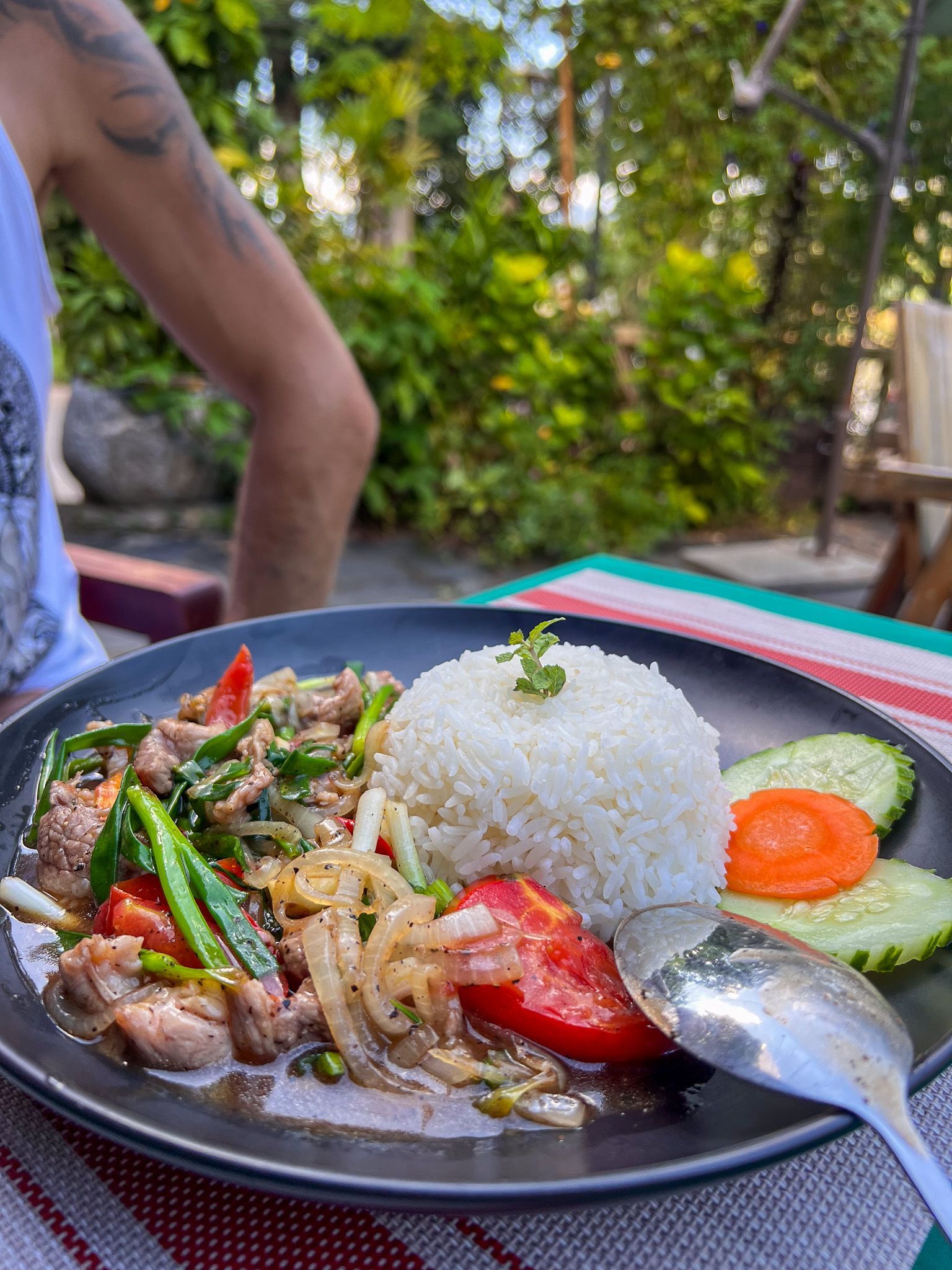 Porcja tajskiego dania z wołowiną, cebulą, pomidorami, warzywami i ryżem, podana na czarnym talerzu w restauracji na świeżym powietrzu.