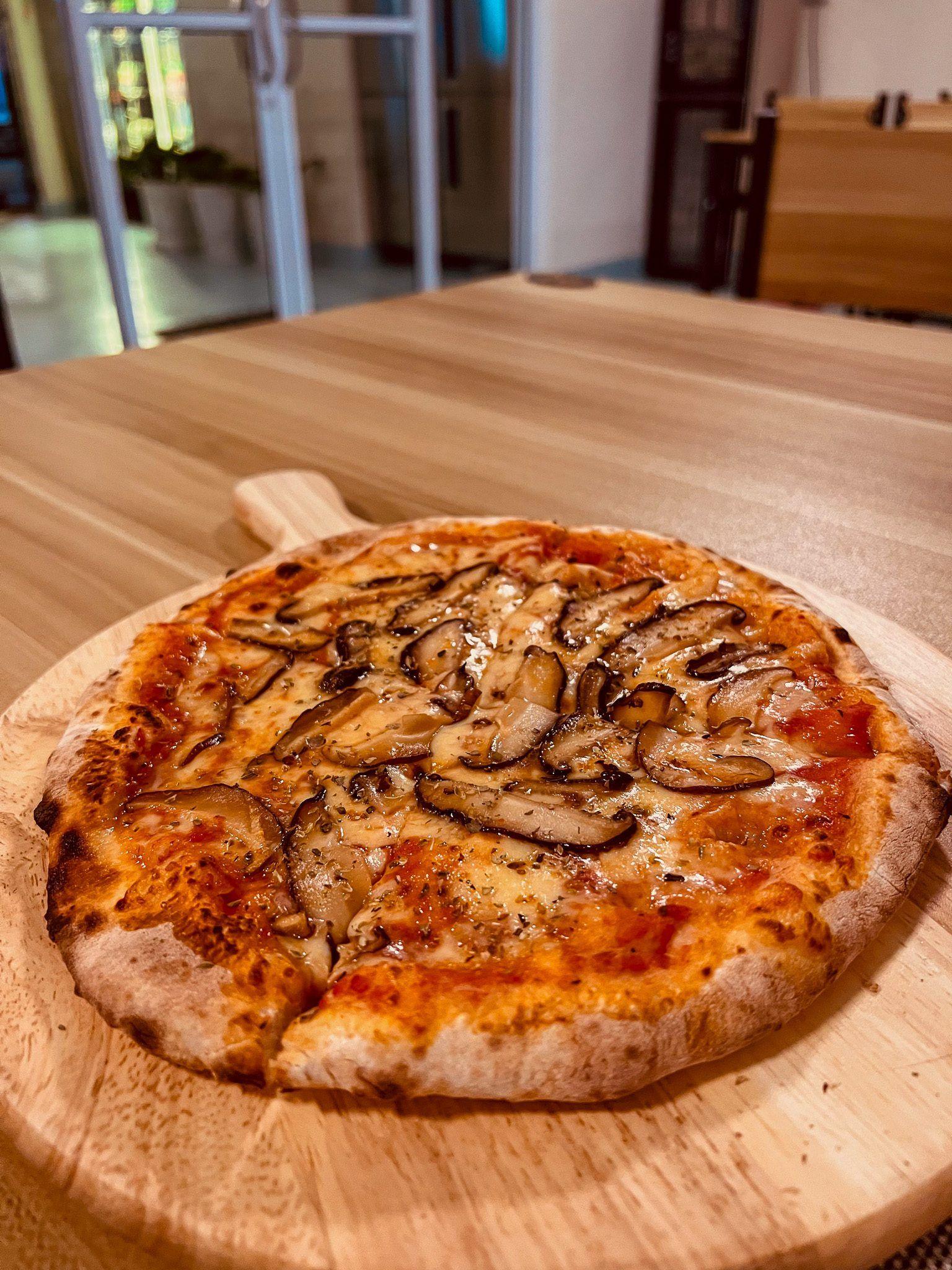 Świeżo upieczona pizza na cienkim cieście, podana na drewnianej desce, z dodatkiem aromatycznych pieczarek i roztopionego sera.