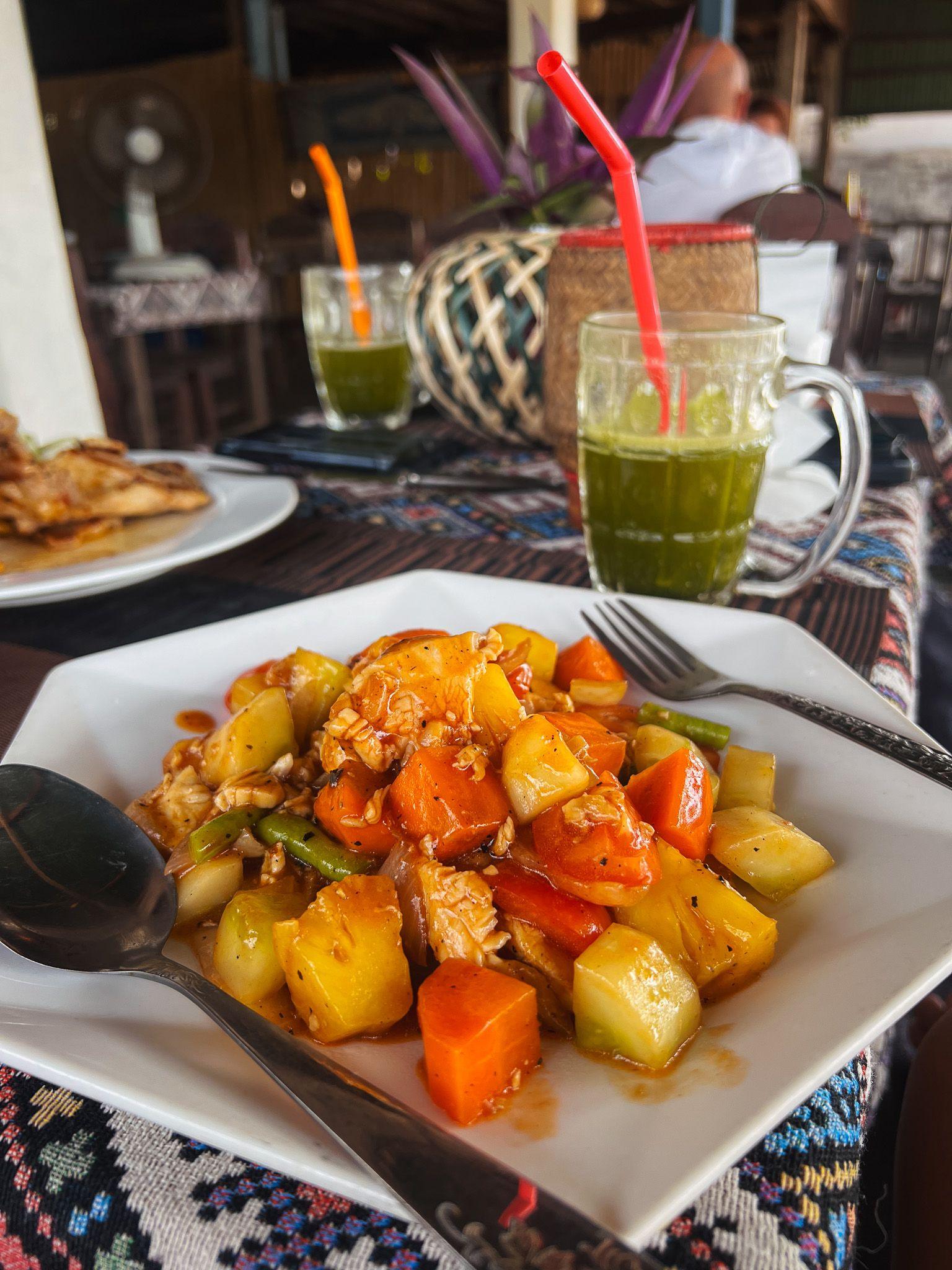 Kolorowe danie kuchni laotańskiej – kurczak z warzywami i ananasem w sosie, podane na białym talerzu.