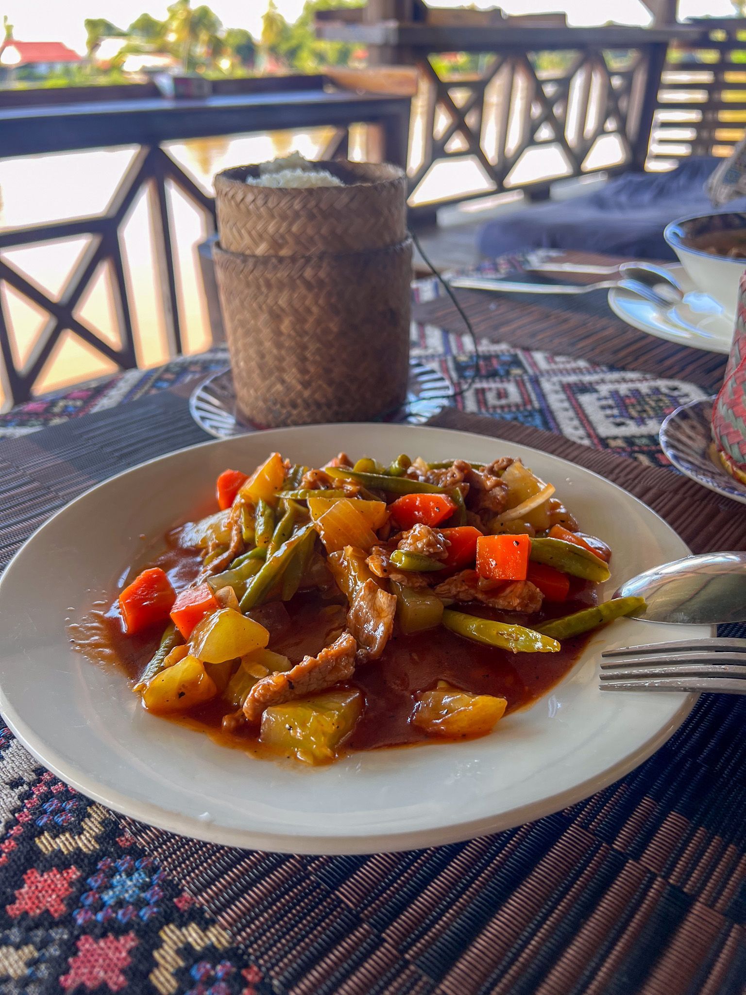 Talerz z wołowiną smażoną z warzywami w sosie słodko-kwaśnym, podany z kleistym ryżem w tradycyjnym koszyku, w restauracji nad brzegiem Mekongu.