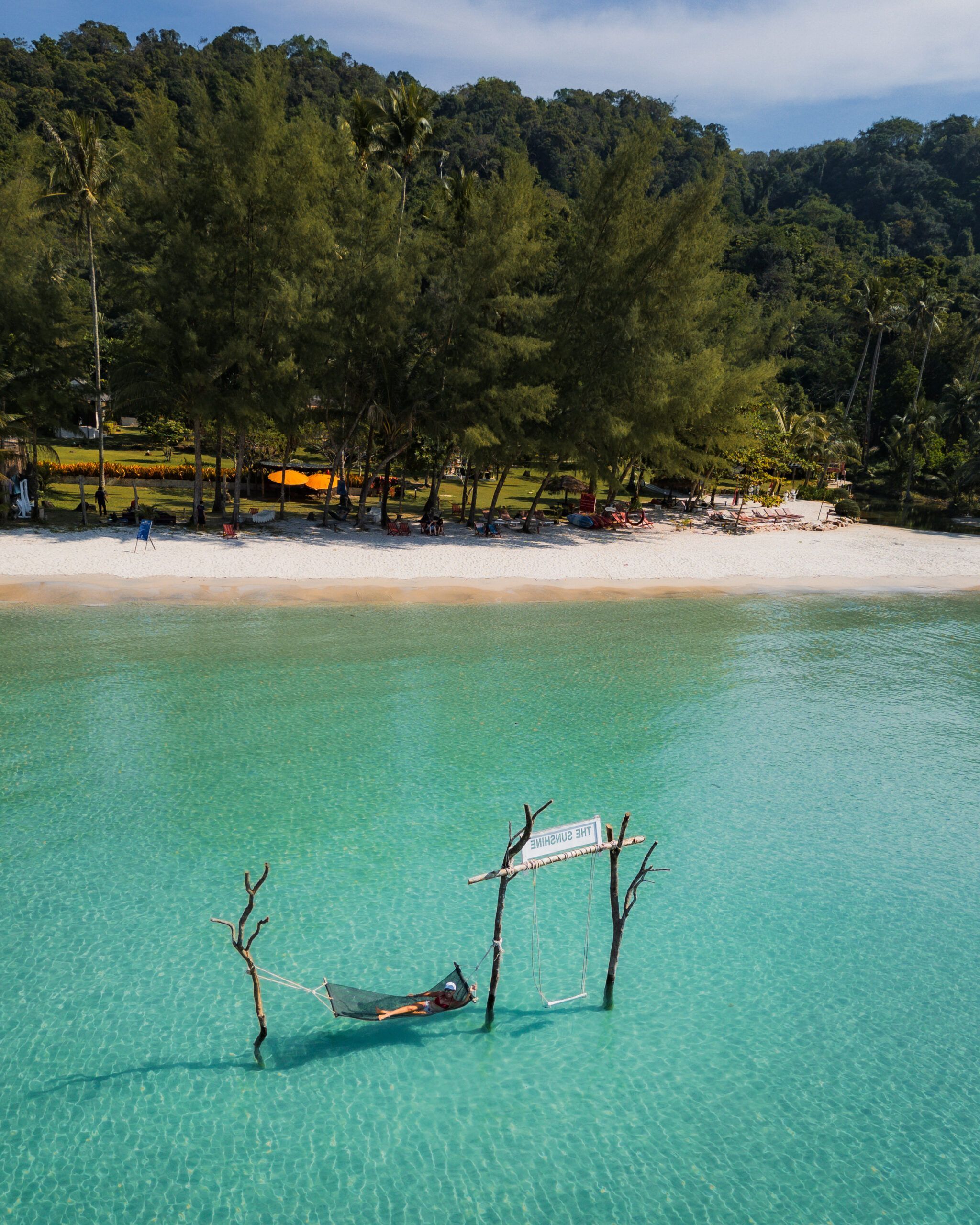Osoba relaksująca się w hamaku zawieszonym nad turkusową wodą w pobliżu plaży otoczonej lasem palmowym - koh kood - tajlandia