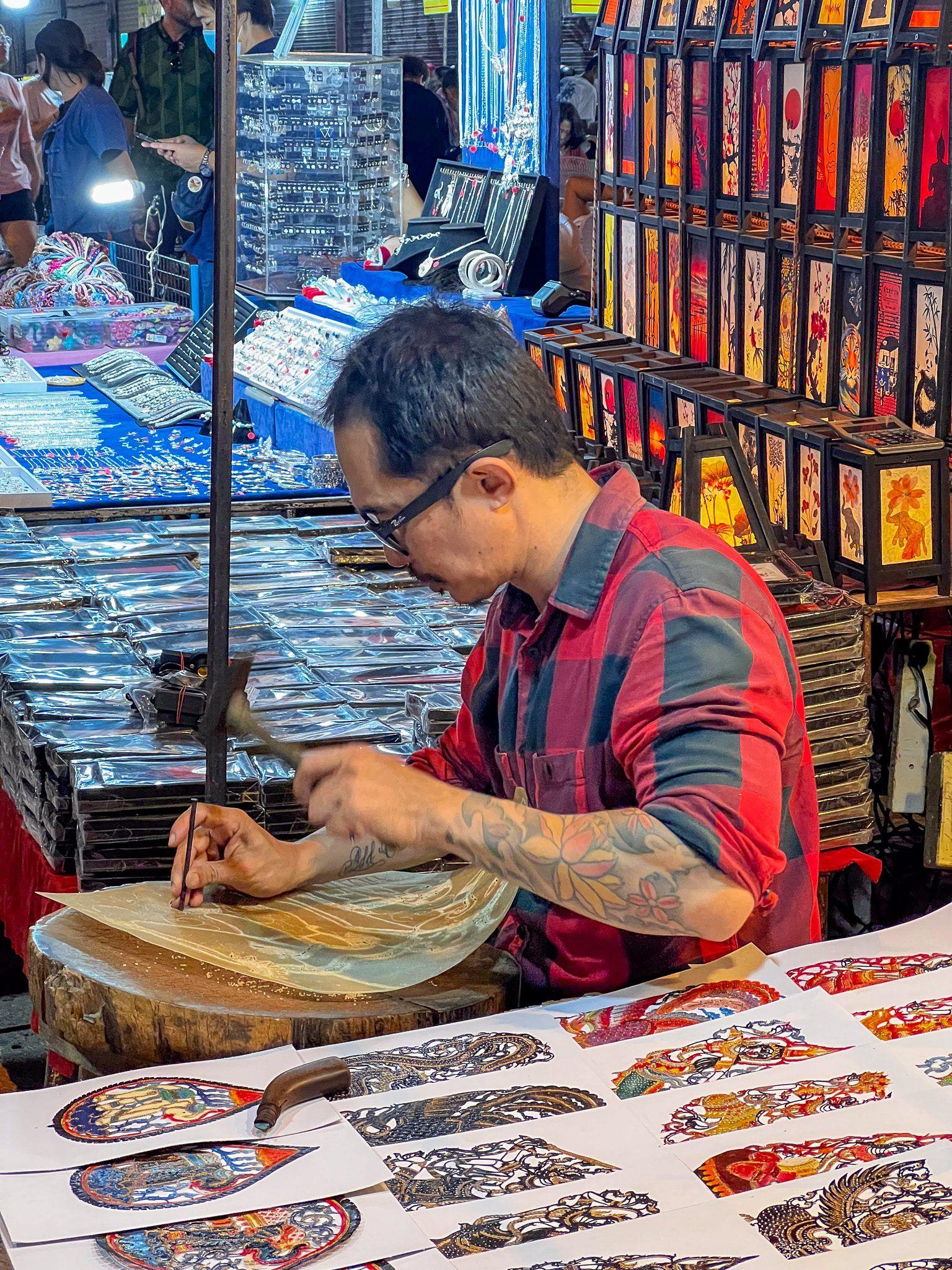 Rzemieślnik tworzący rękodzieło z wycinanki podczas nocnego targu w Azji