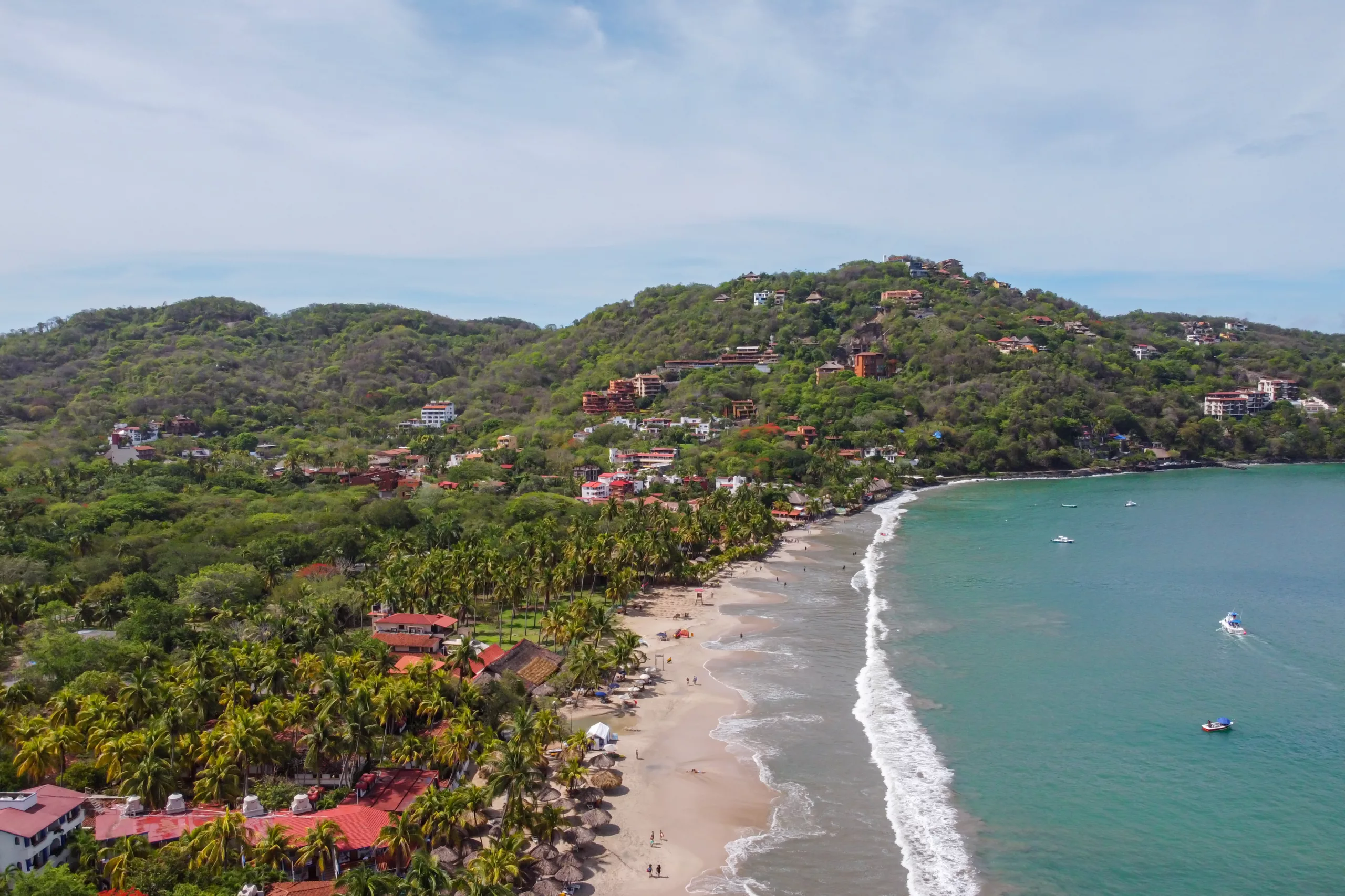 Lotniczy widok na spokojną zatokę z palmami, plażą i zielonymi wzgórzami na wybrzeżu Pacyfiku w Zihuatanejo, Meksyk