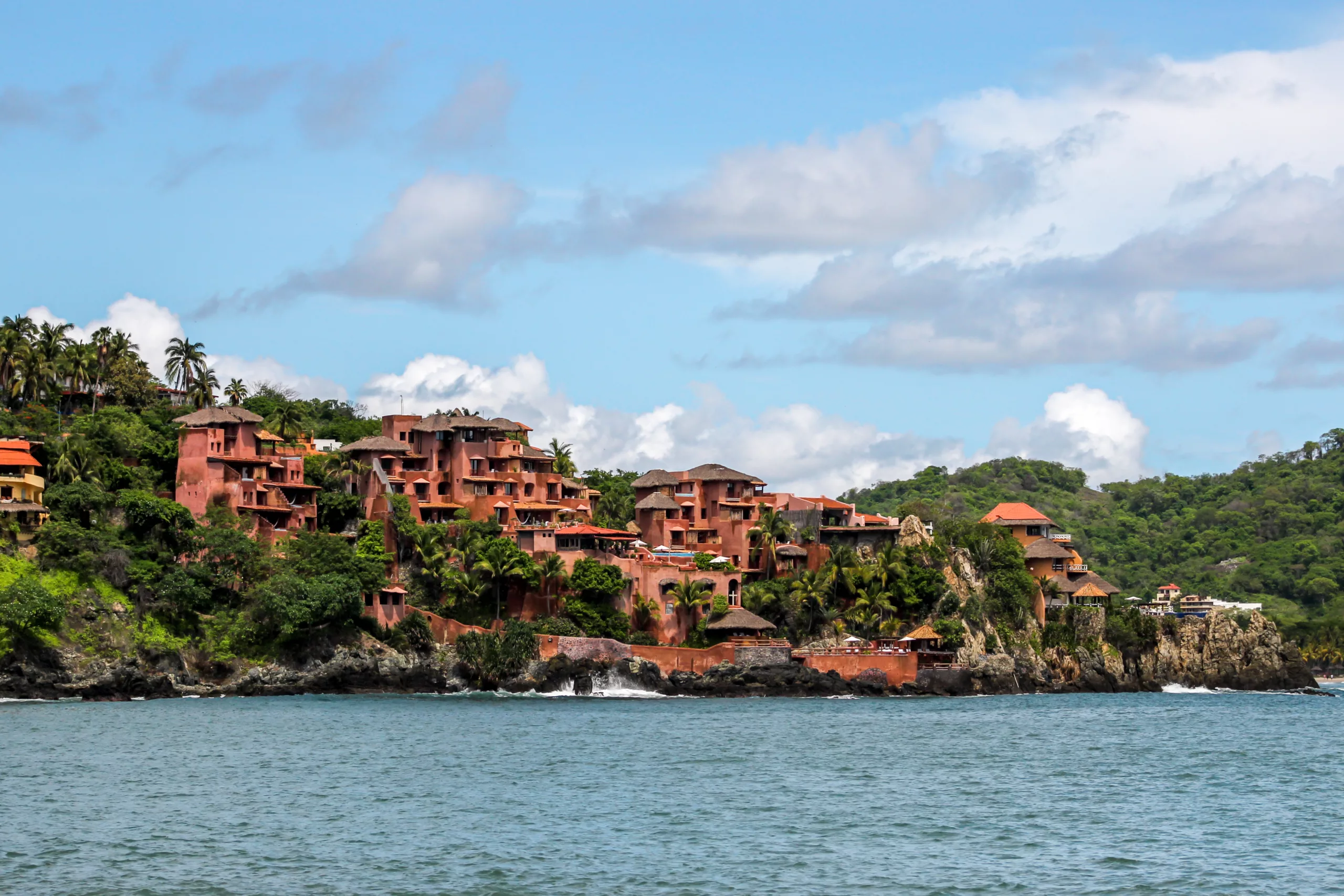 Malownicze różowo-czerwone budynki położone na skalistym klifie nad brzegiem oceanu w Meksyku, otoczone tropikalną zielenią