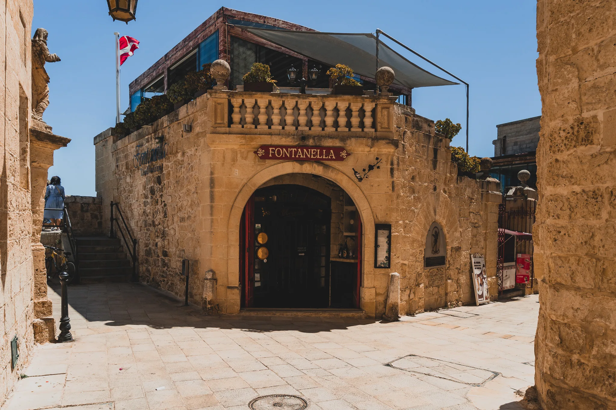 Wejście do słynnej kawiarni Fontanella w Mdinie na Malcie z widoczną kamienną fasadą i czerwonym szyldem