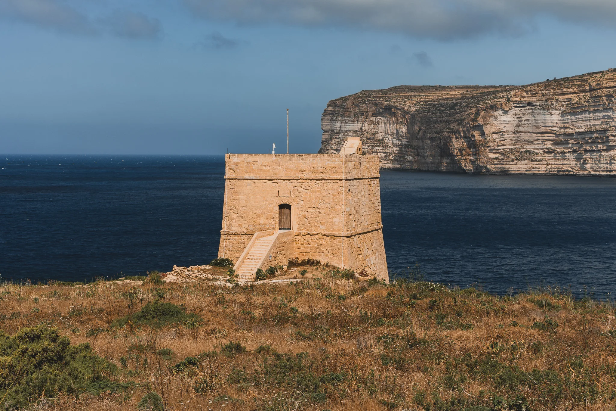 Wieża obronna Dwejra Tower na klifowym wybrzeżu Gozo z widokiem na morze i skaliste urwiska