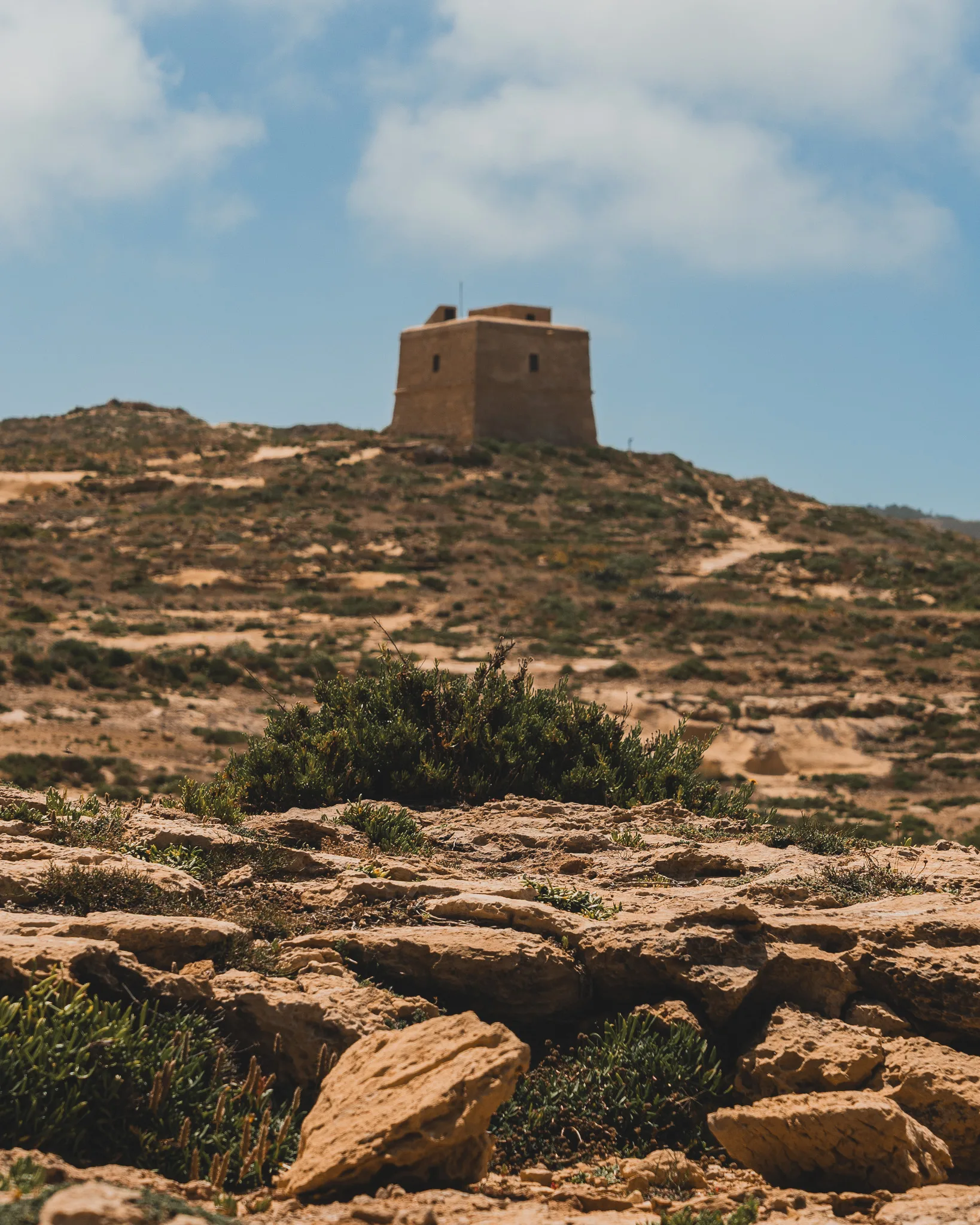 Samotna wieża strażnicza na wzgórzu Gozo, otoczona suchym, kamienistym krajobrazem i niską roślinnością