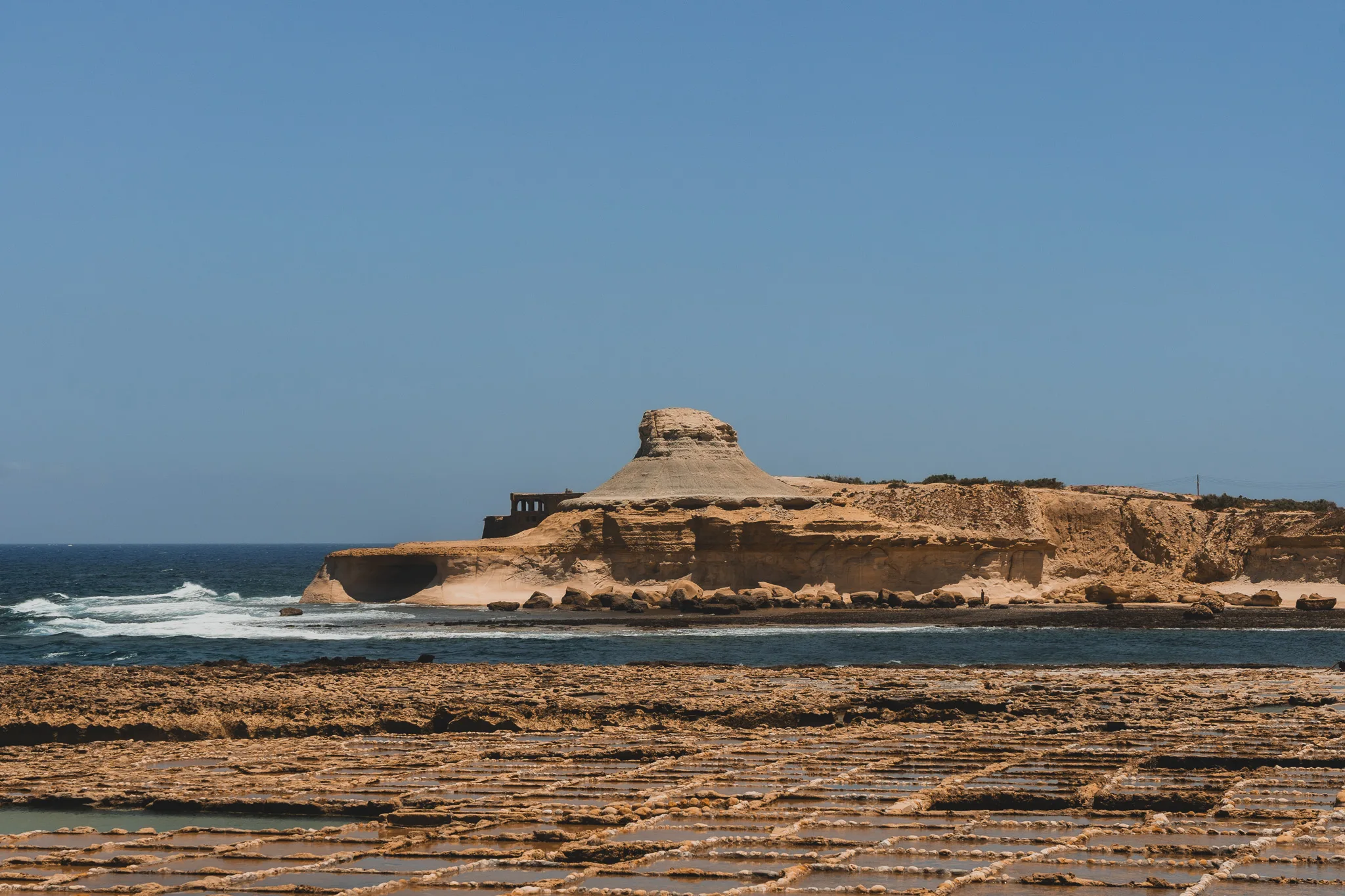 Pola solne na Gozo z charakterystycznym stożkowatym wzgórzem na tle lazurowego morza