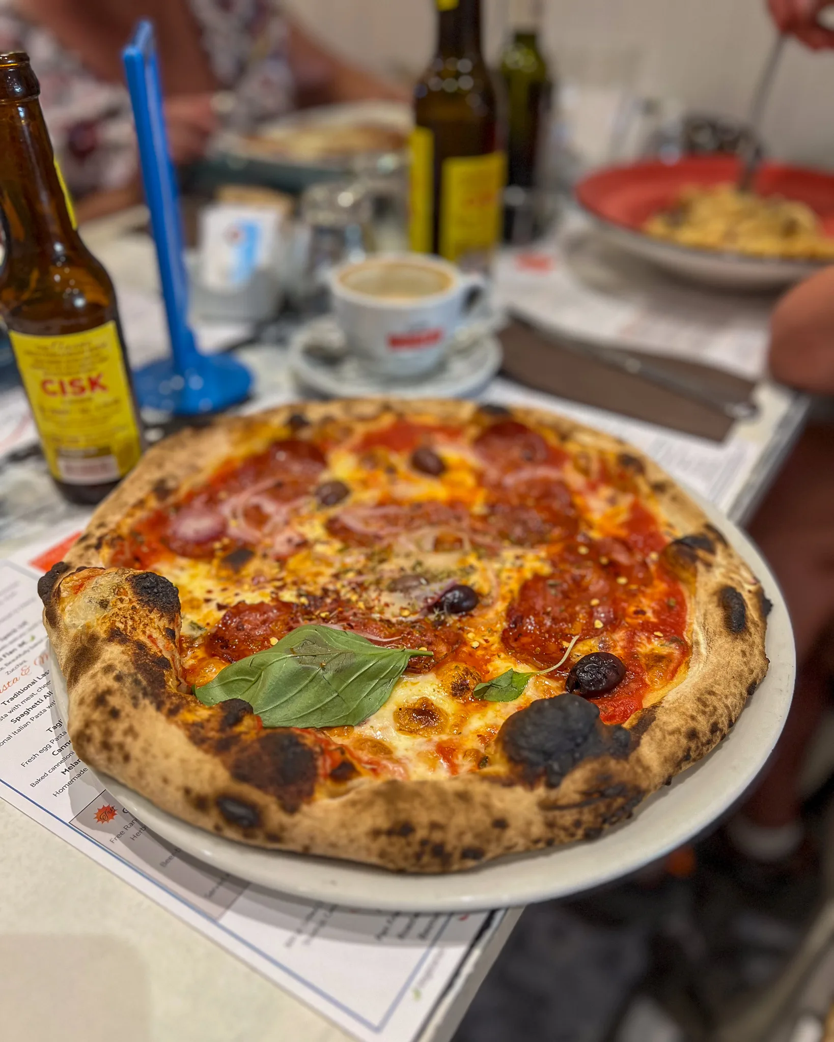 Włoska pizza z salami, oliwkami, cebulą i bazylią na cienkim cieście, podana w restauracji z lokalnym piwem Cisk