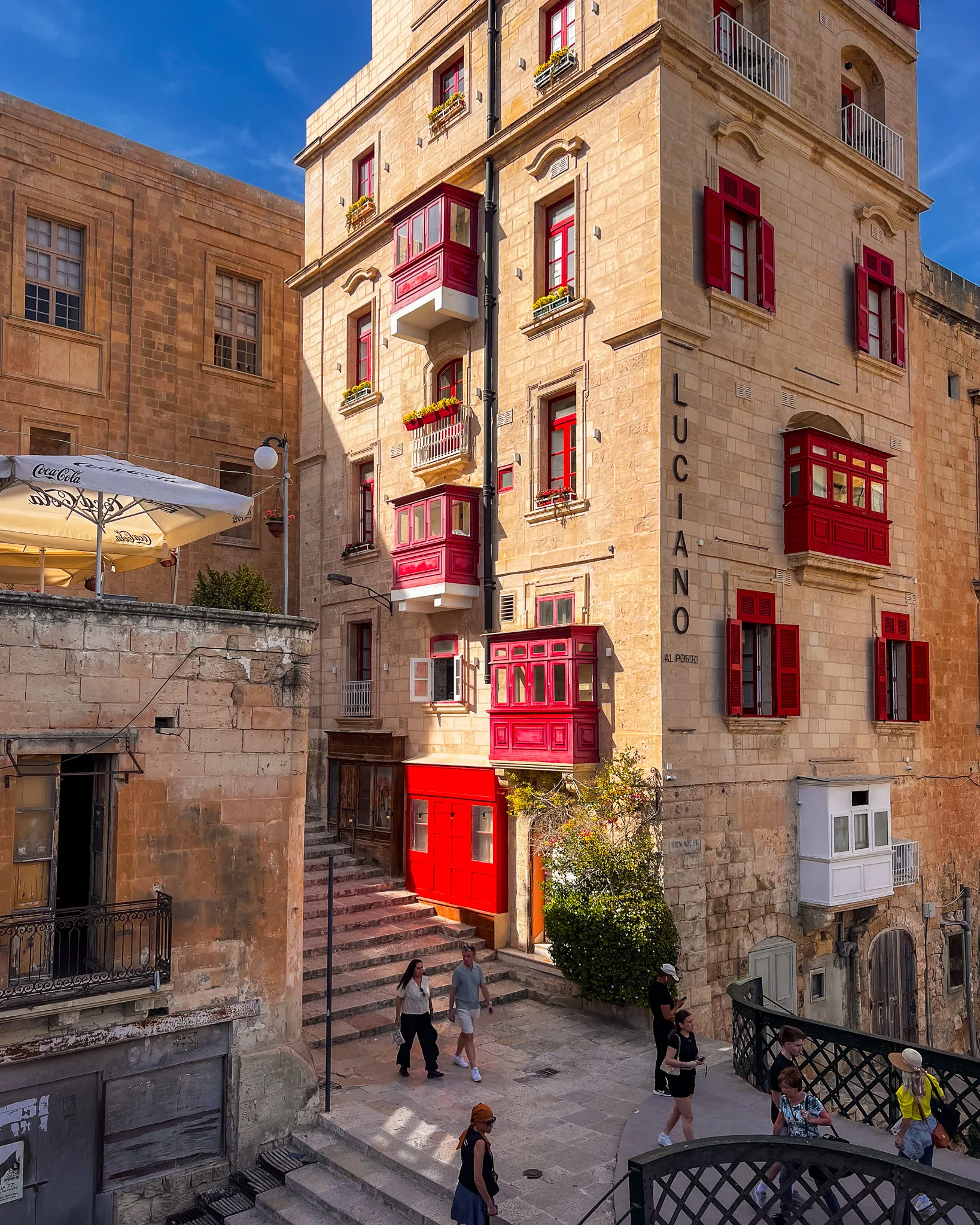 Kamienica z czerwonymi balkonami i okiennicami przy uliczce w Valletcie – Luciano Al Porto, Malta
