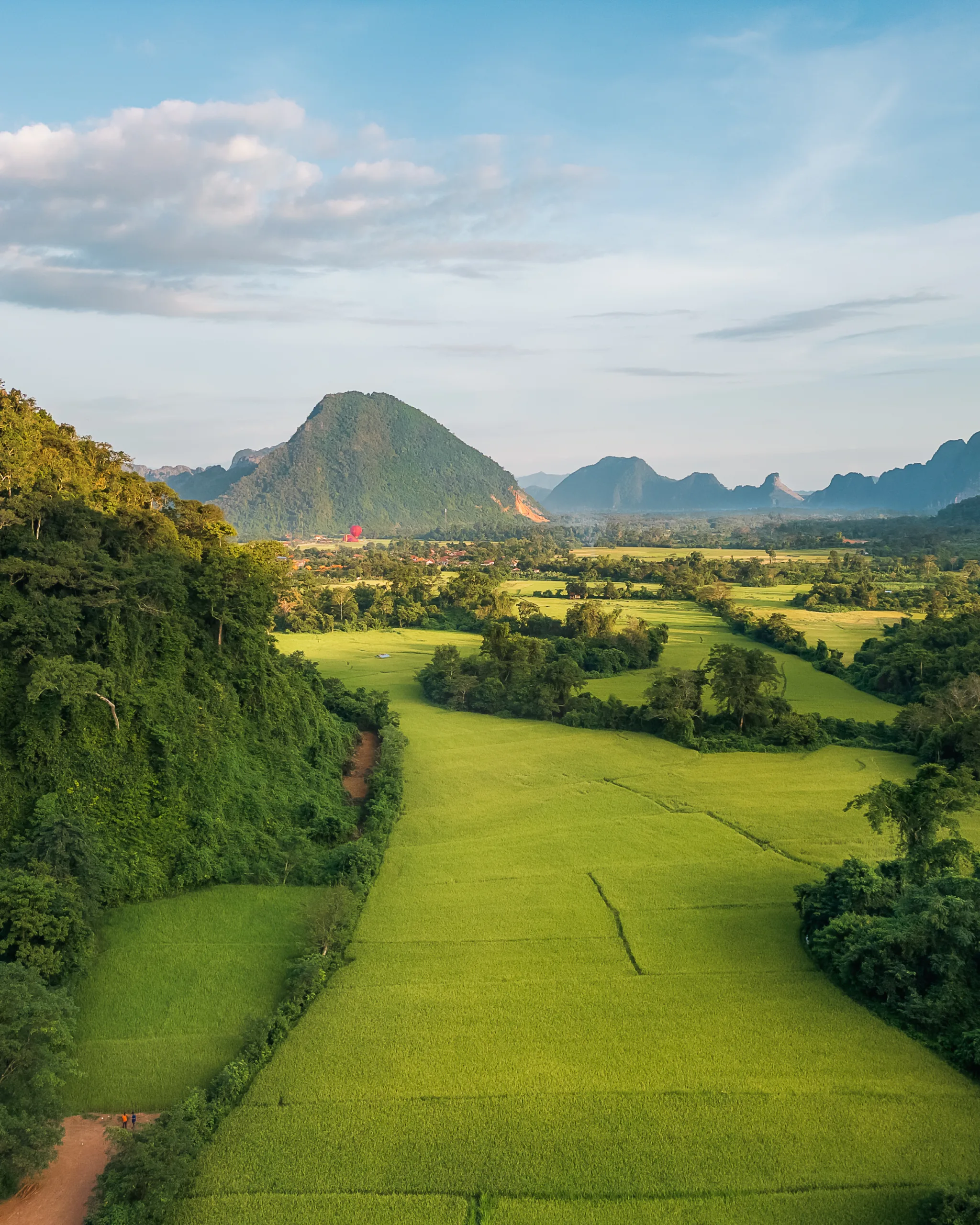 Panorama zielonych pól ryżowych otoczonych wzgórzami i górami w okolicach Vang Vieng, Laos.