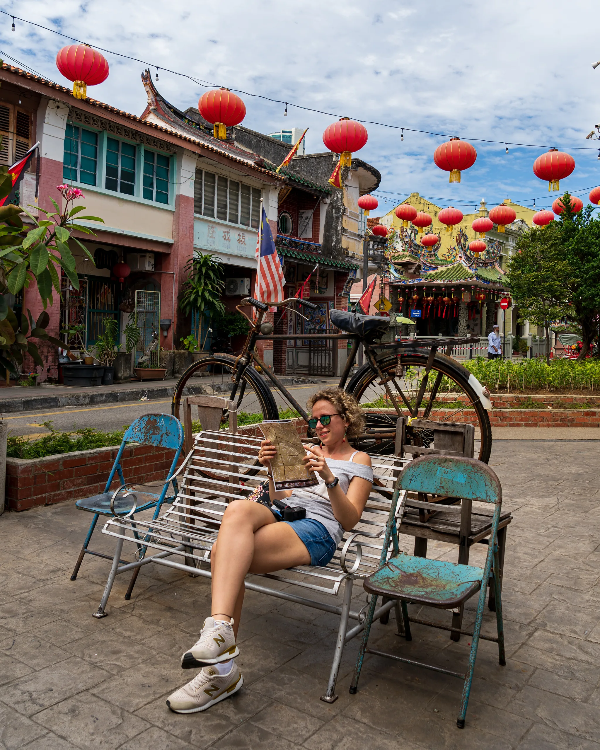 Turystka siedzi na ławce z mapą w ręku w kolonialnej dzielnicy Georgetown na Penang, otoczona chińskimi lampionami i zabytkowymi budynkami - co zobaczyć w malezji