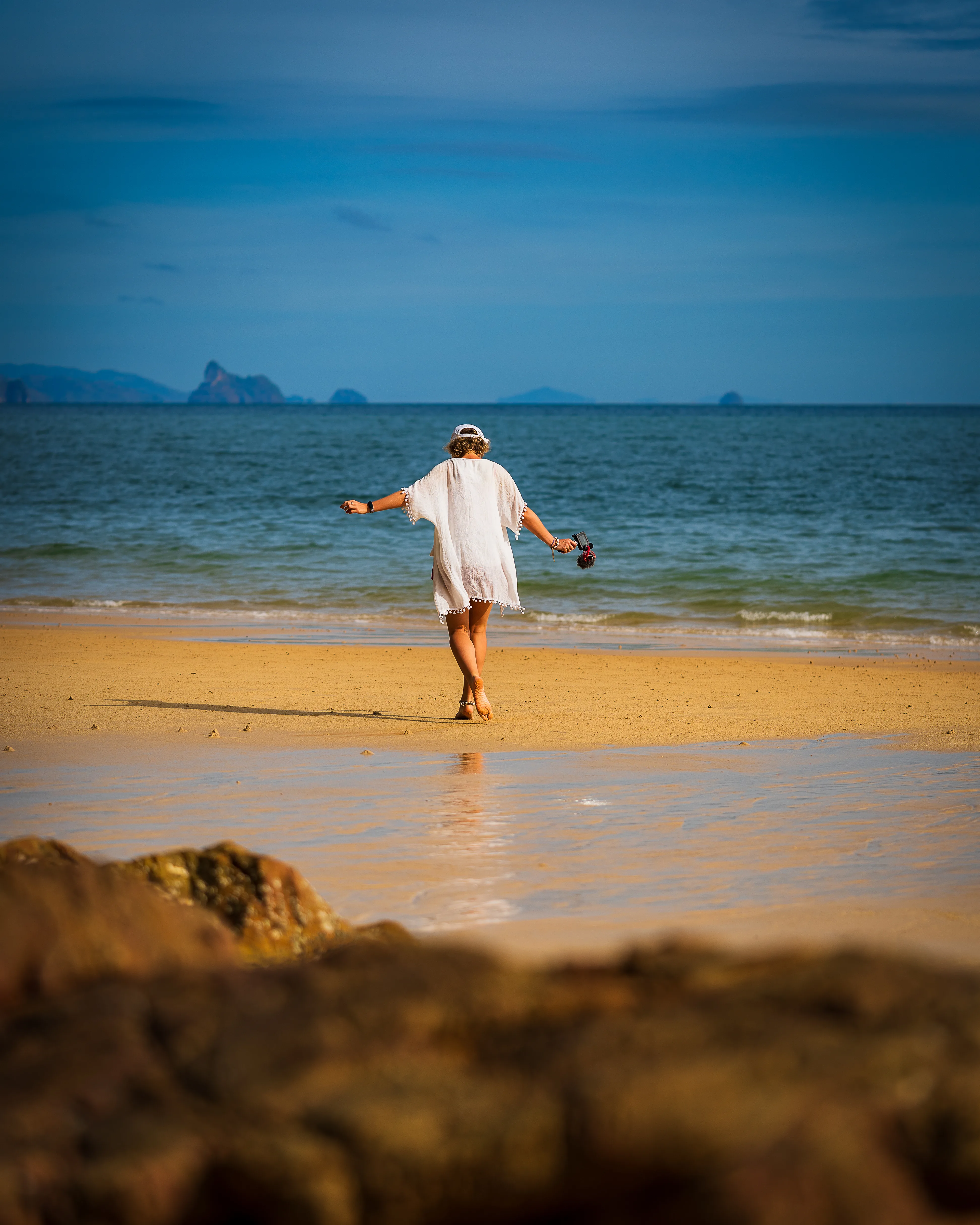 Podróżniczka idąca po piaszczystej plaży na Langkawi w Malezji, z morzem i górzystymi wyspami na horyzoncie.
