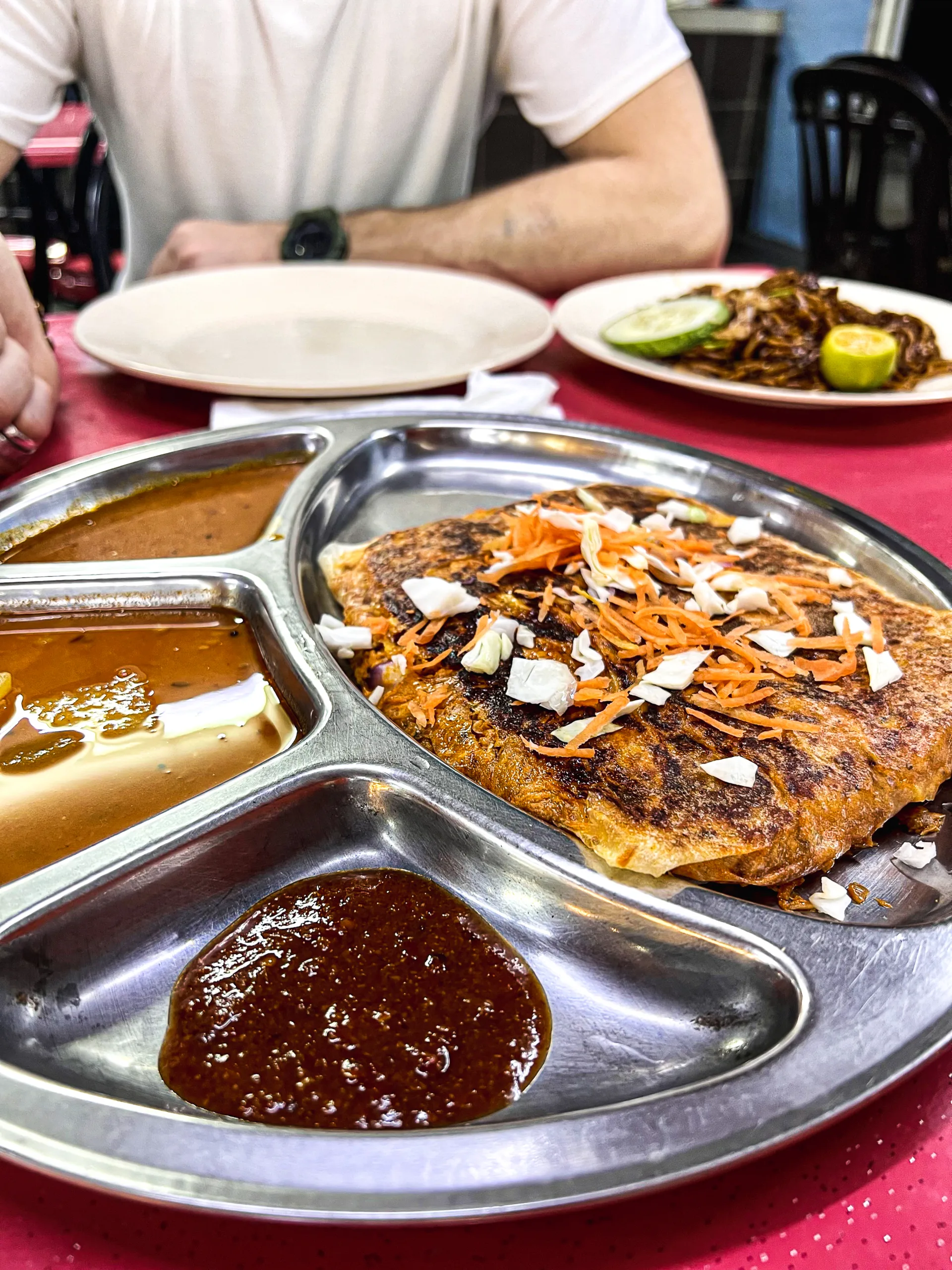 Roti – malezyjski placek nadziewany mięsem i warzywami, podany z sosami curry i chili na metalowej tacy